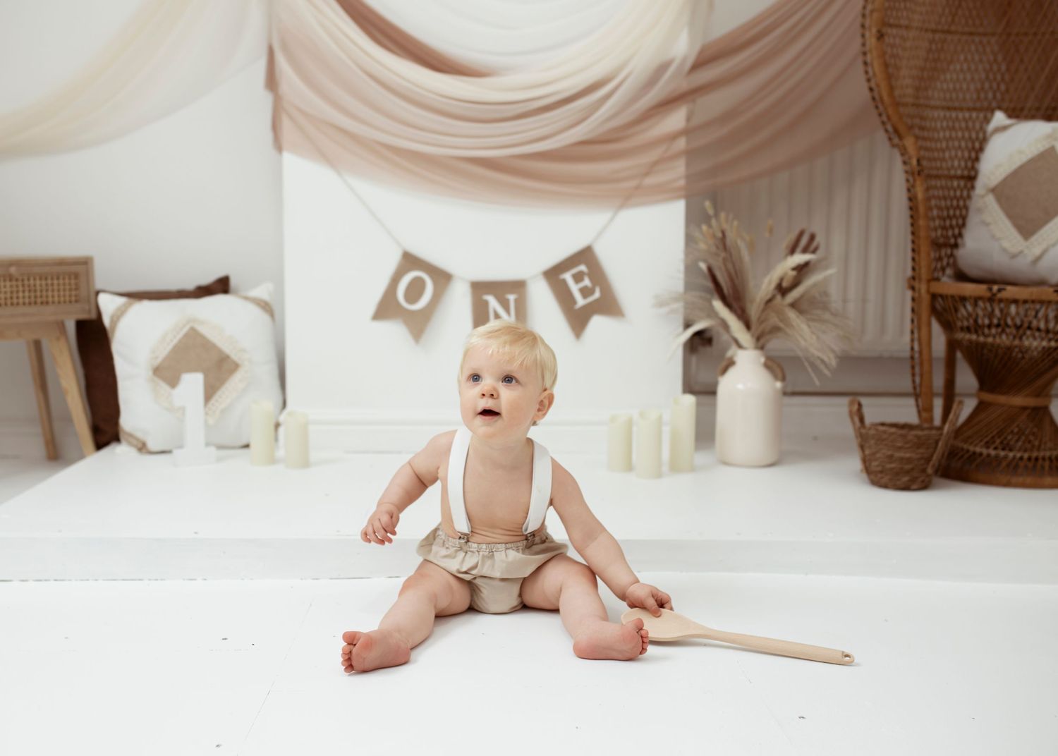 Minimalist first birthday setup with white backdrop and brown banner decorations.