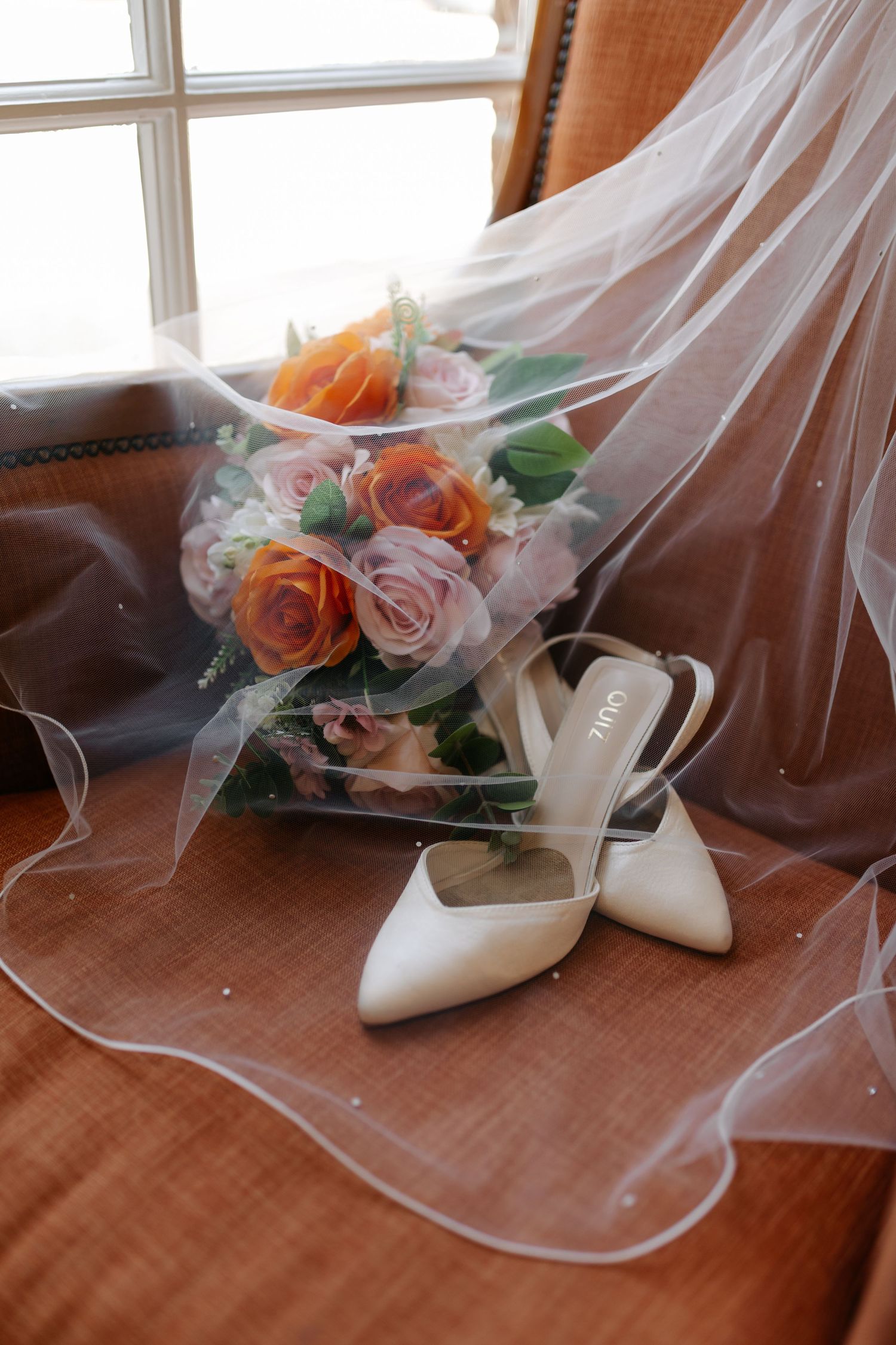 Wedding details with white shoes, veil and orange roses on brown surface.