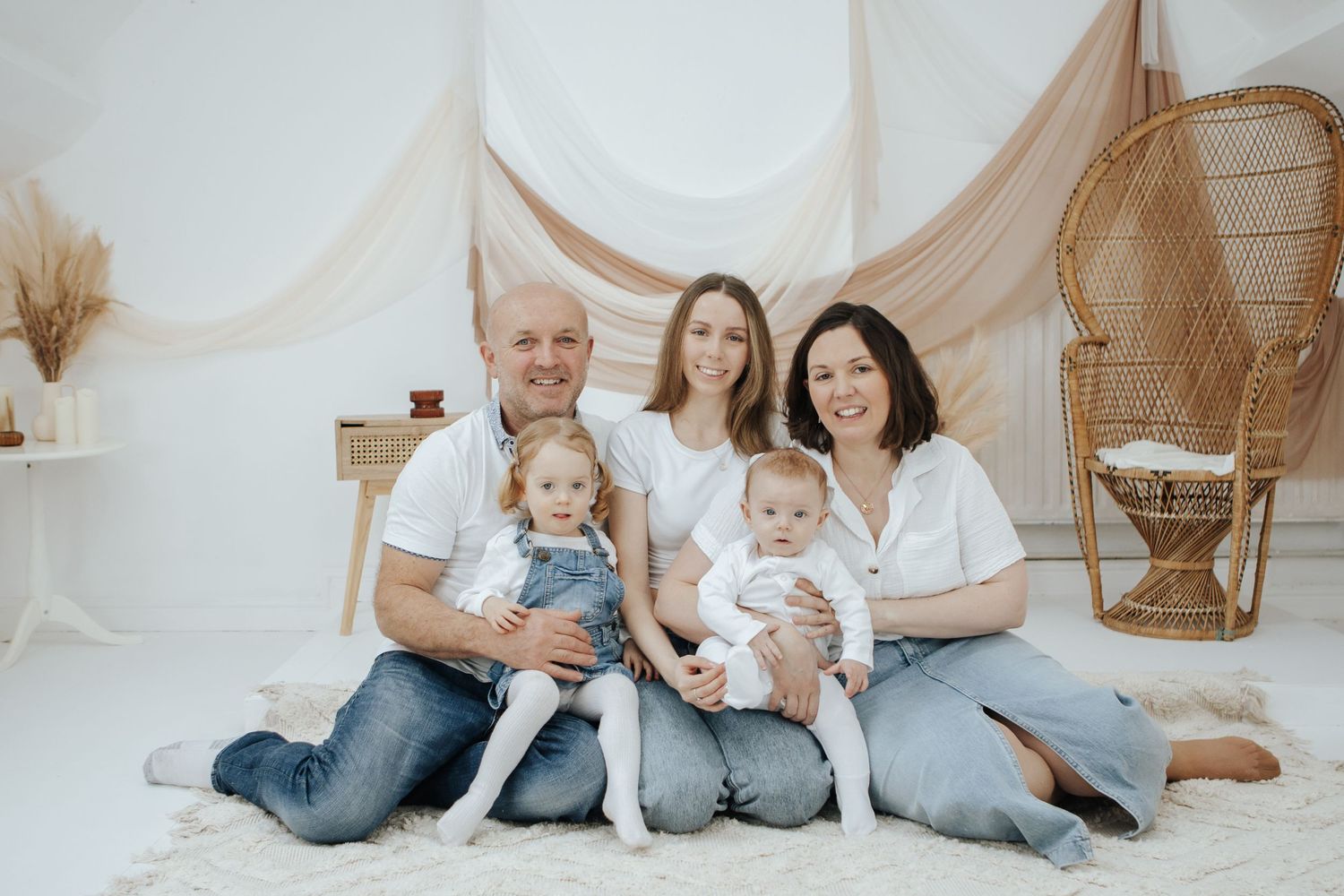 Family portrait session with matching casual outfits against a neutral backdrop.