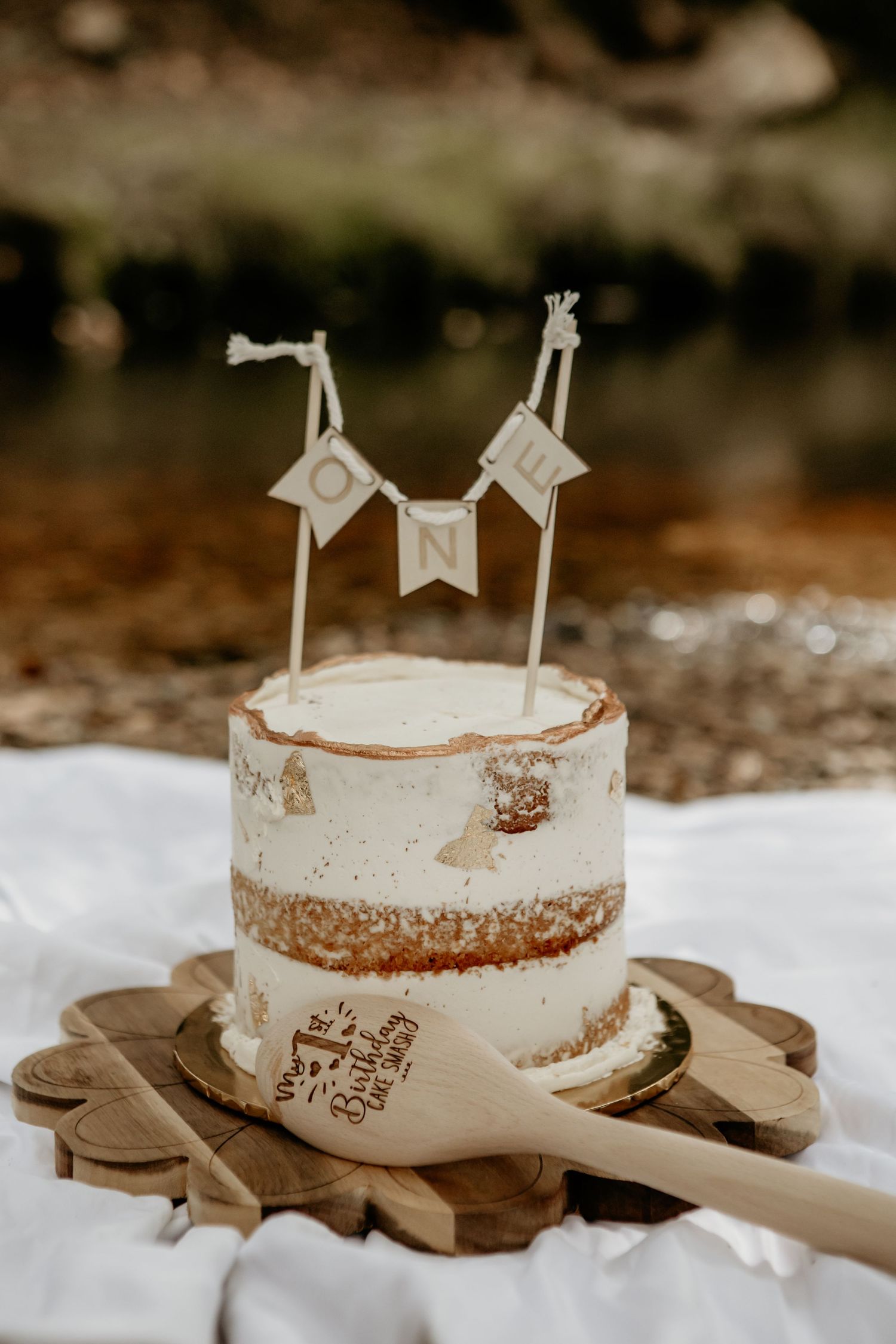 Rustic white birthday cake with banner flags displayed on wooden board outdoors.