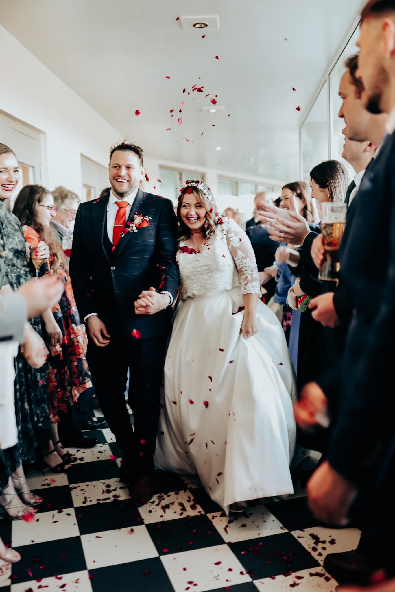 Wedding celebration with red confetti being thrown in an indoor venue with black and white checkered floor.