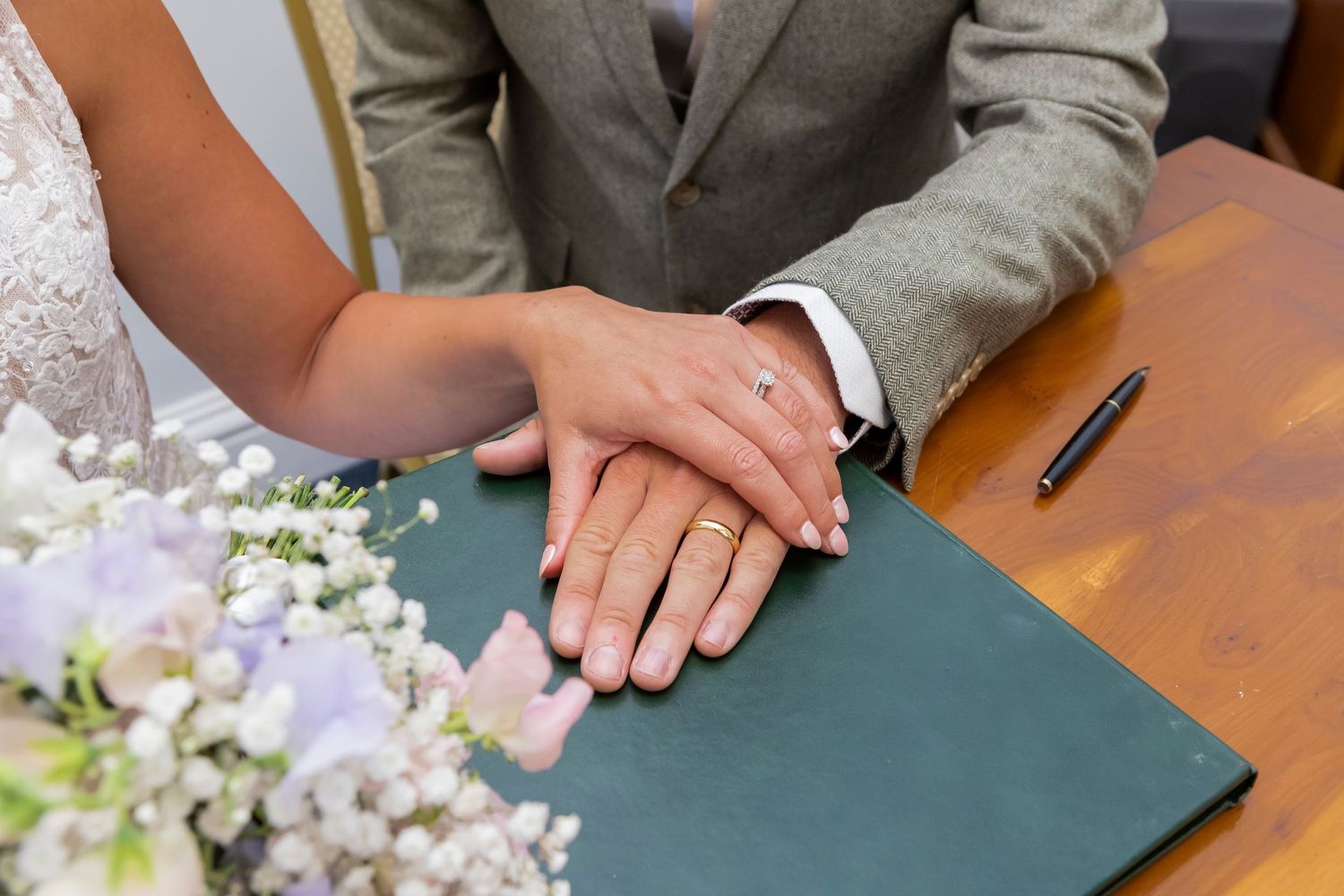 Close-up of hands signing wedding documents on a green table.