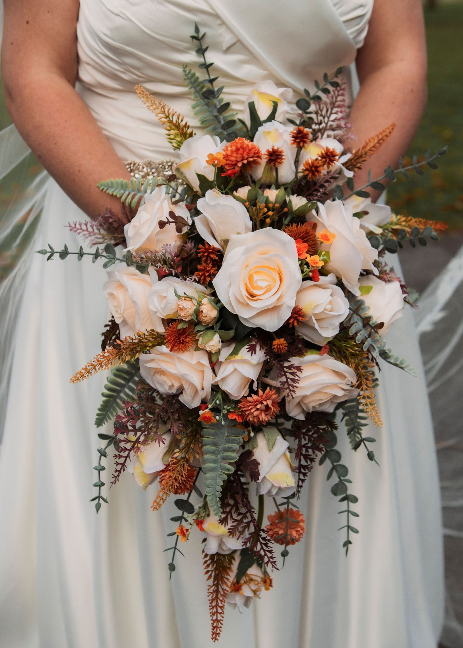 Beautiful fall-themed wedding bouquet with peach roses, orange accents, and eucalyptus greenery.