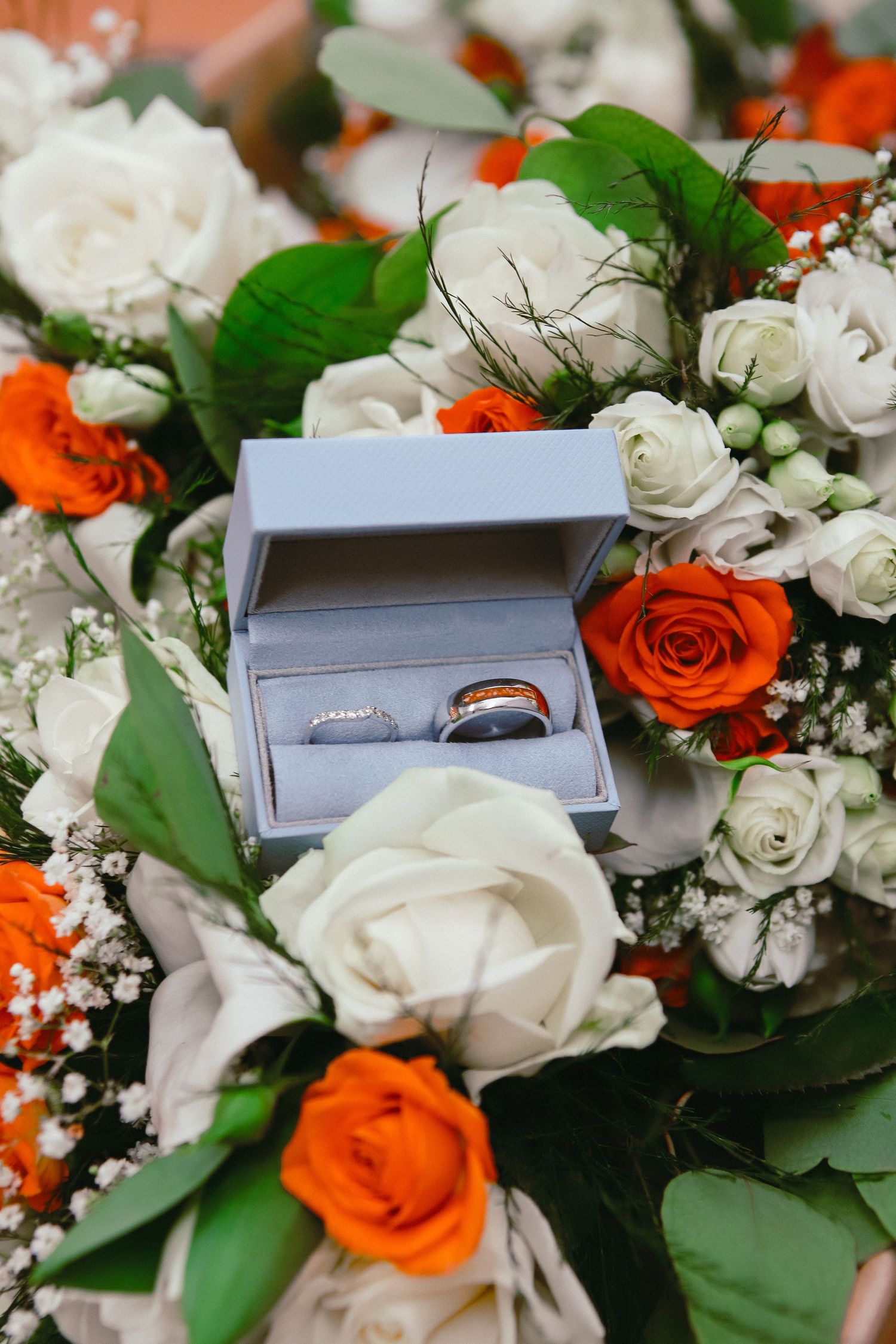 Wedding rings displayed in gray box surrounded by orange and white roses.