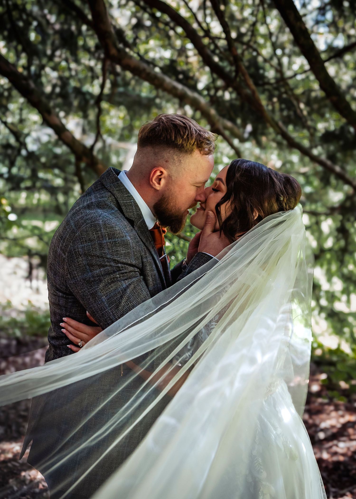 Intimate wedding portraits under tree branches with flowing white veil creating a romantic atmosphere.