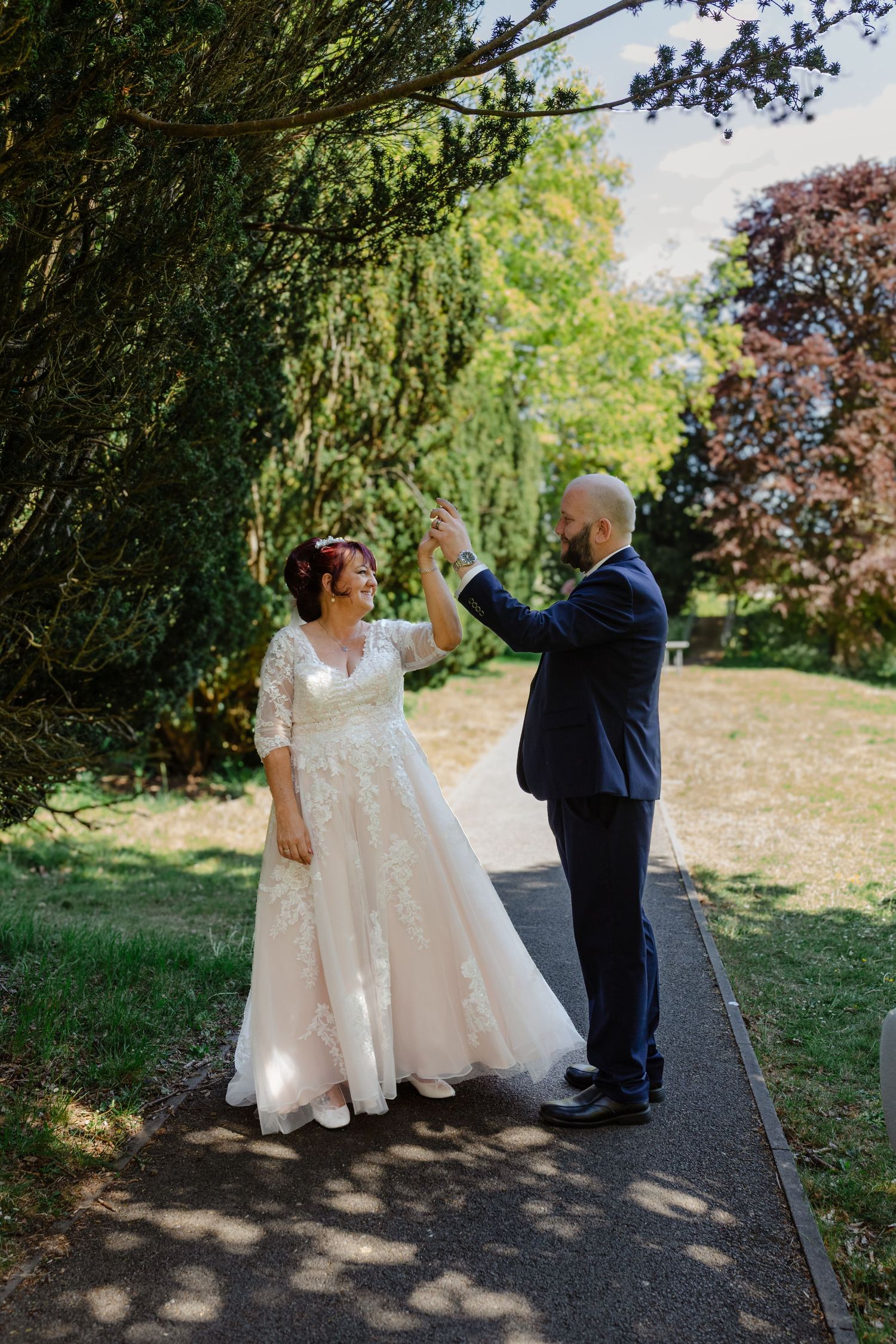 Wedding couple dancing and twirling together on outdoor path surrounded by trees.