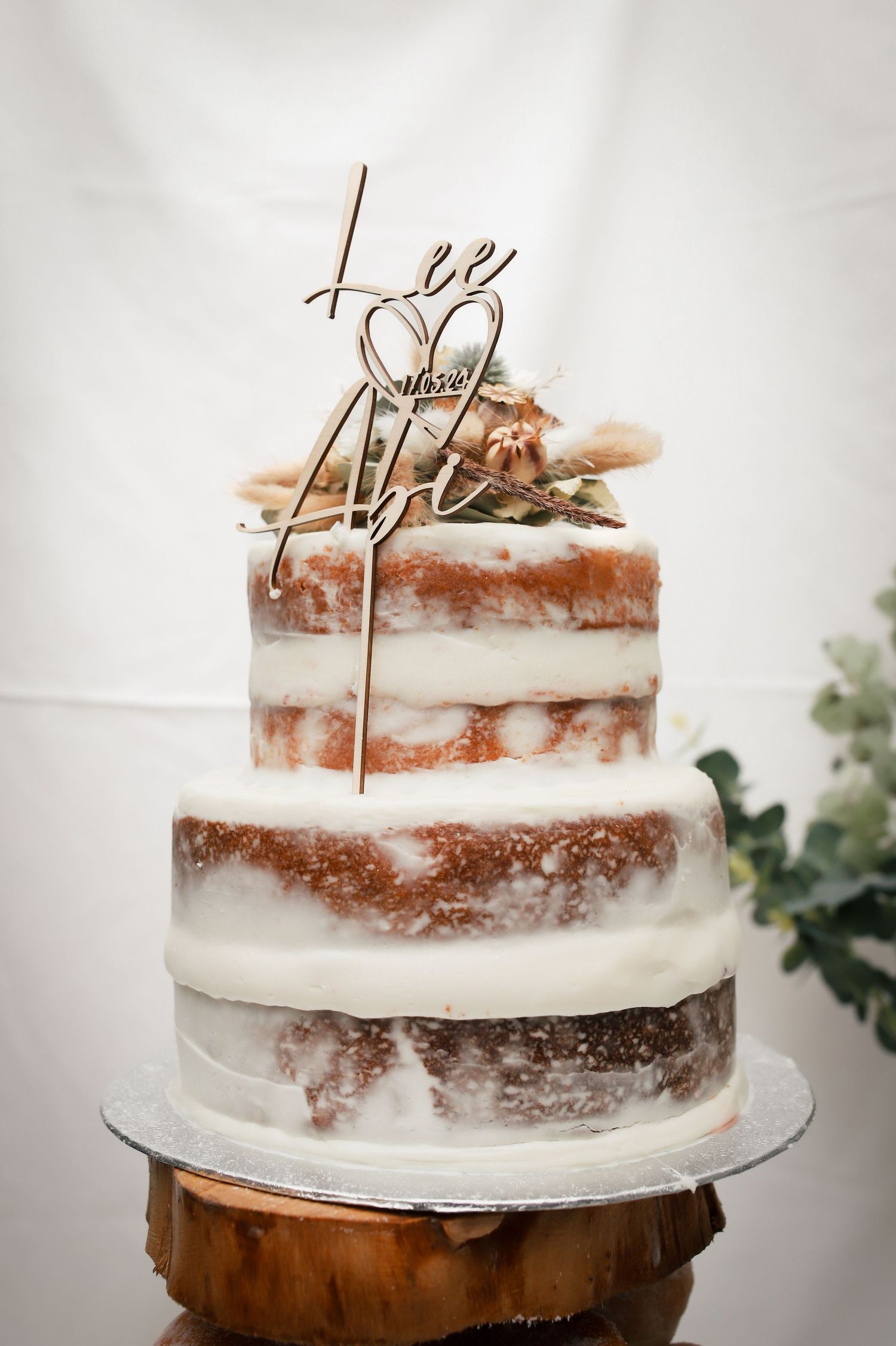 Semi-naked wedding cake with rustic wooden cake topper on white backdrop.