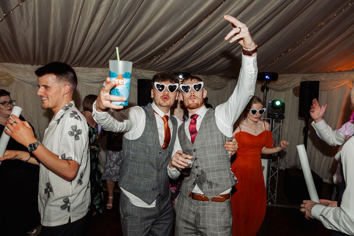 Wedding reception dance party with guests in formal attire enjoying themselves under ambient lighting.