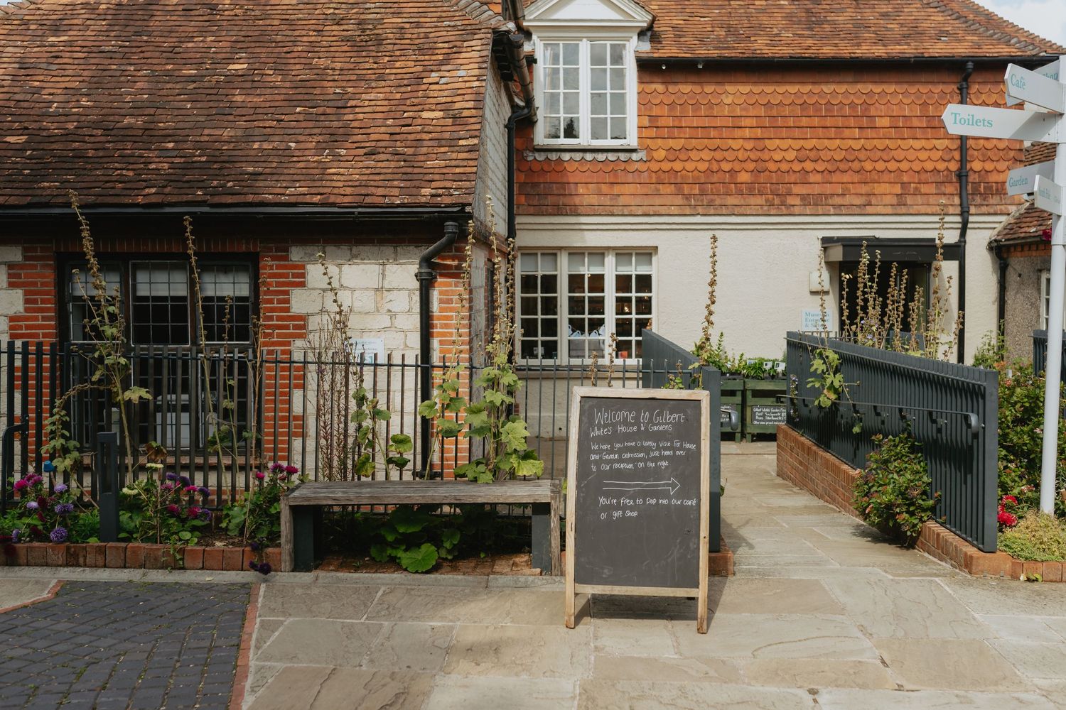 Charming exterior of a traditional English cottage with terracotta roof tiles and a chalkboard sign by the entrance.