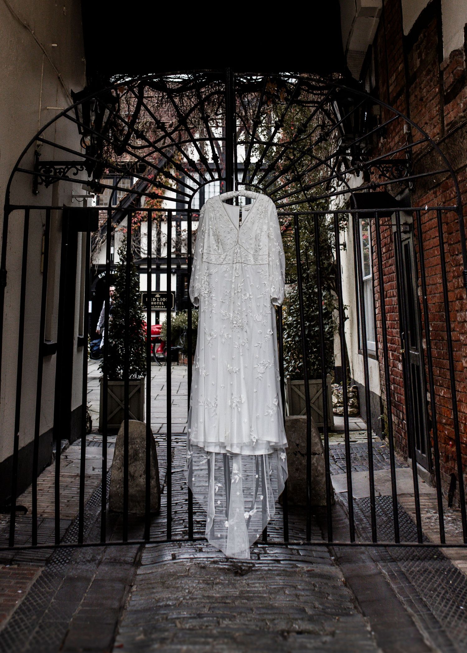 White wedding dress hanging in a brick archway with wrought iron gates.