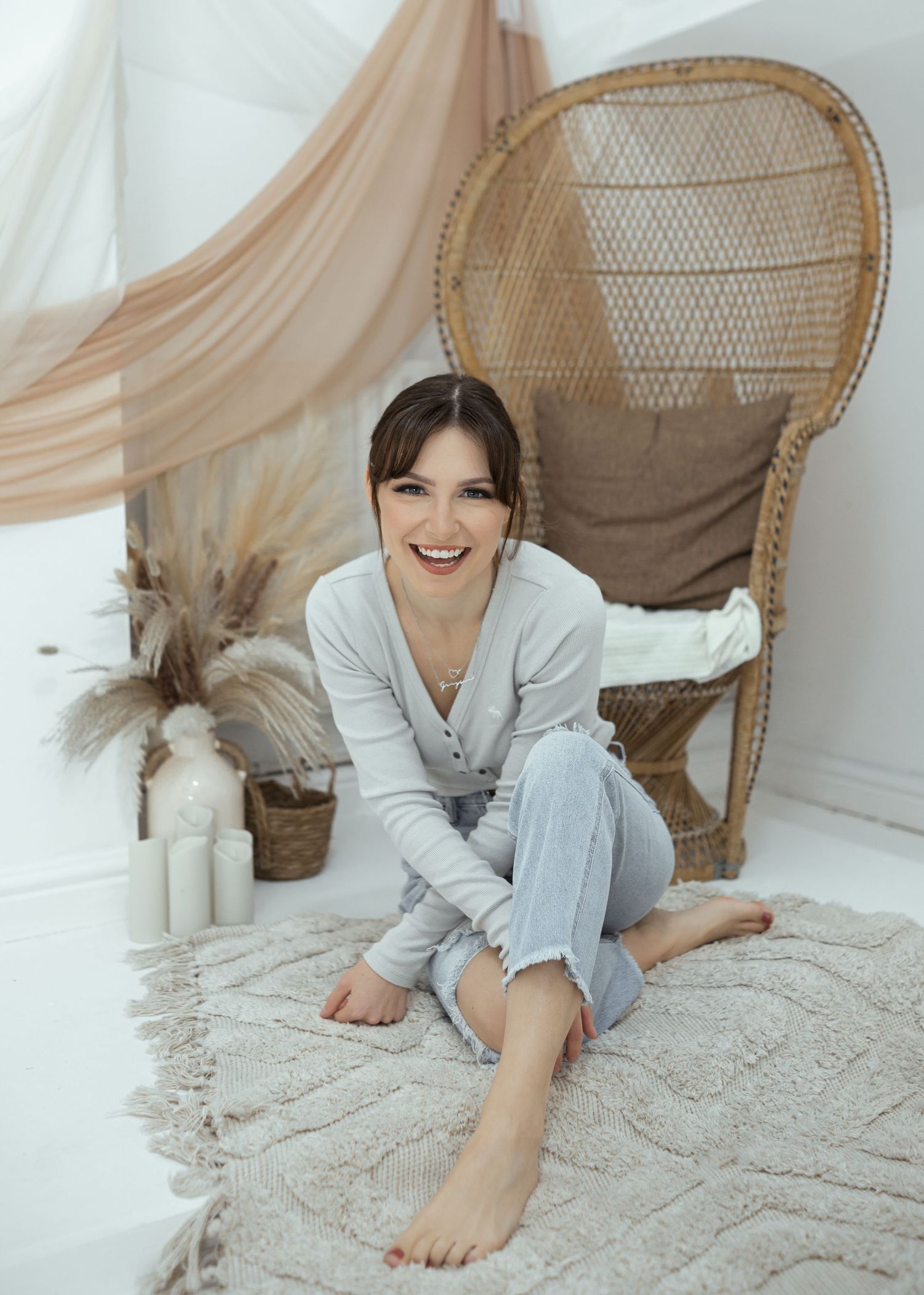 A relaxed person lies on a textured rug wearing casual loungewear near a woven chair.