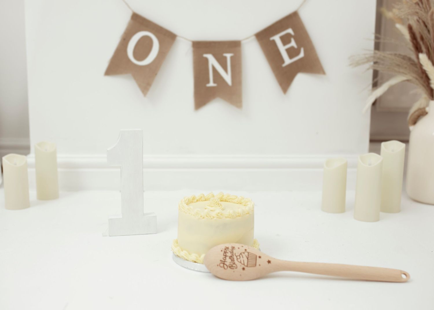 Rustic brown ONE banner with white candles and wooden spoon against light backdrop.