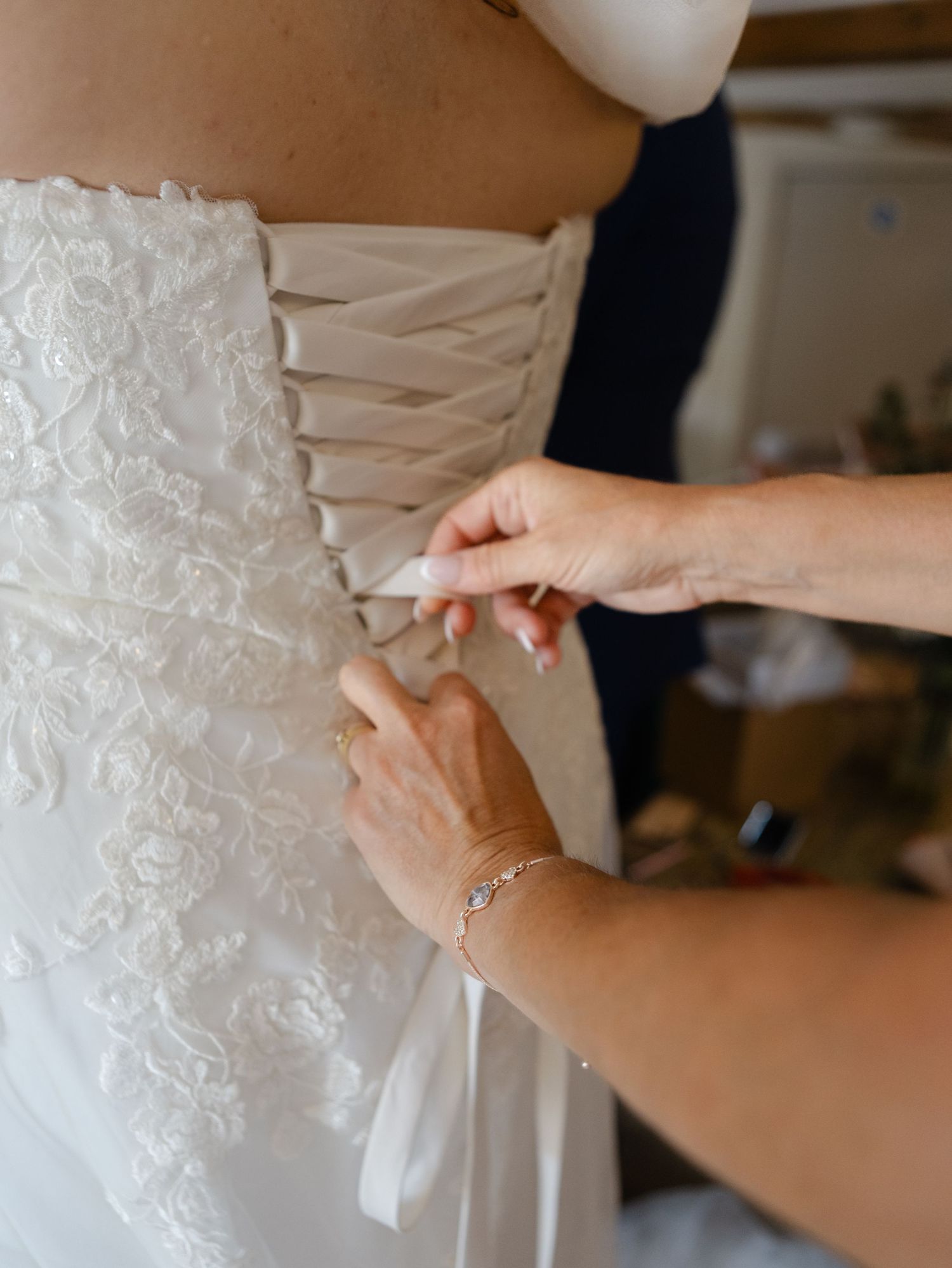 Detailed lace patterns and buttons on a white wedding dress being adjusted.