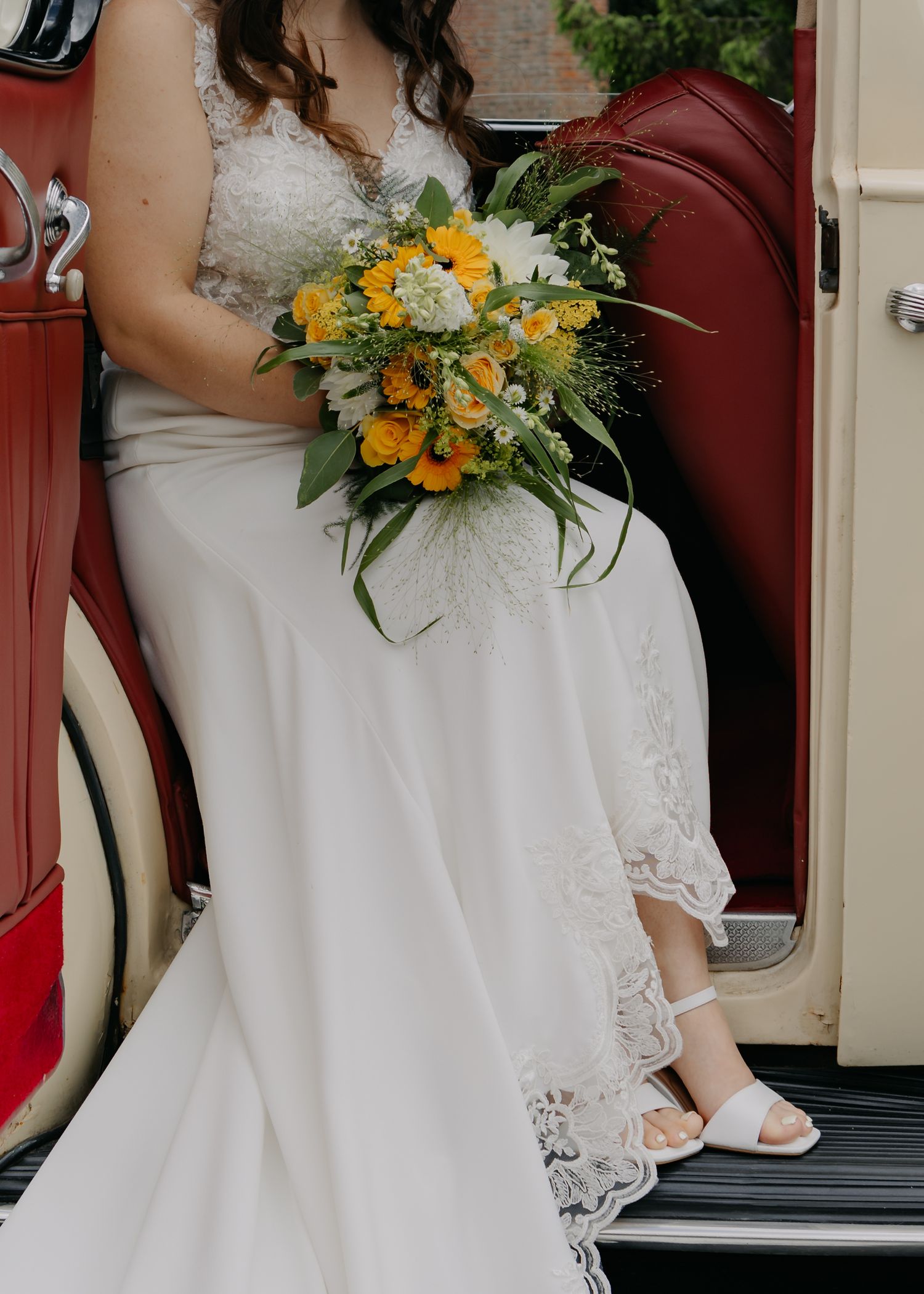 Row of bridesmaids in white dresses holding yellow and orange bouquets.