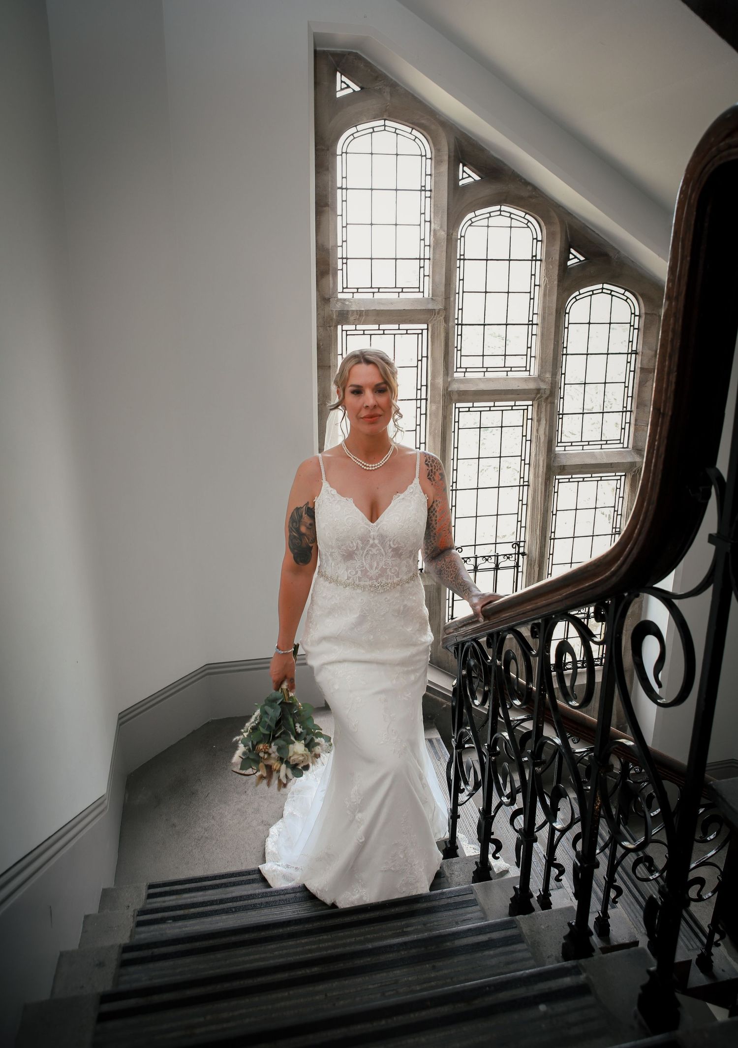 Bride descending grand staircase with beautiful lace train and natural window light.