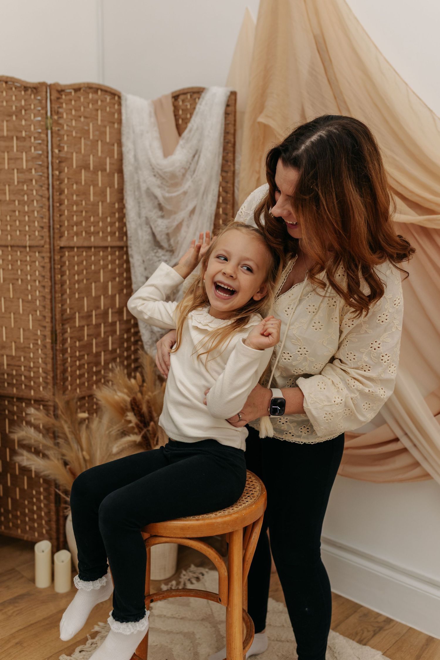Playful family moment captured against beige draped backdrop.