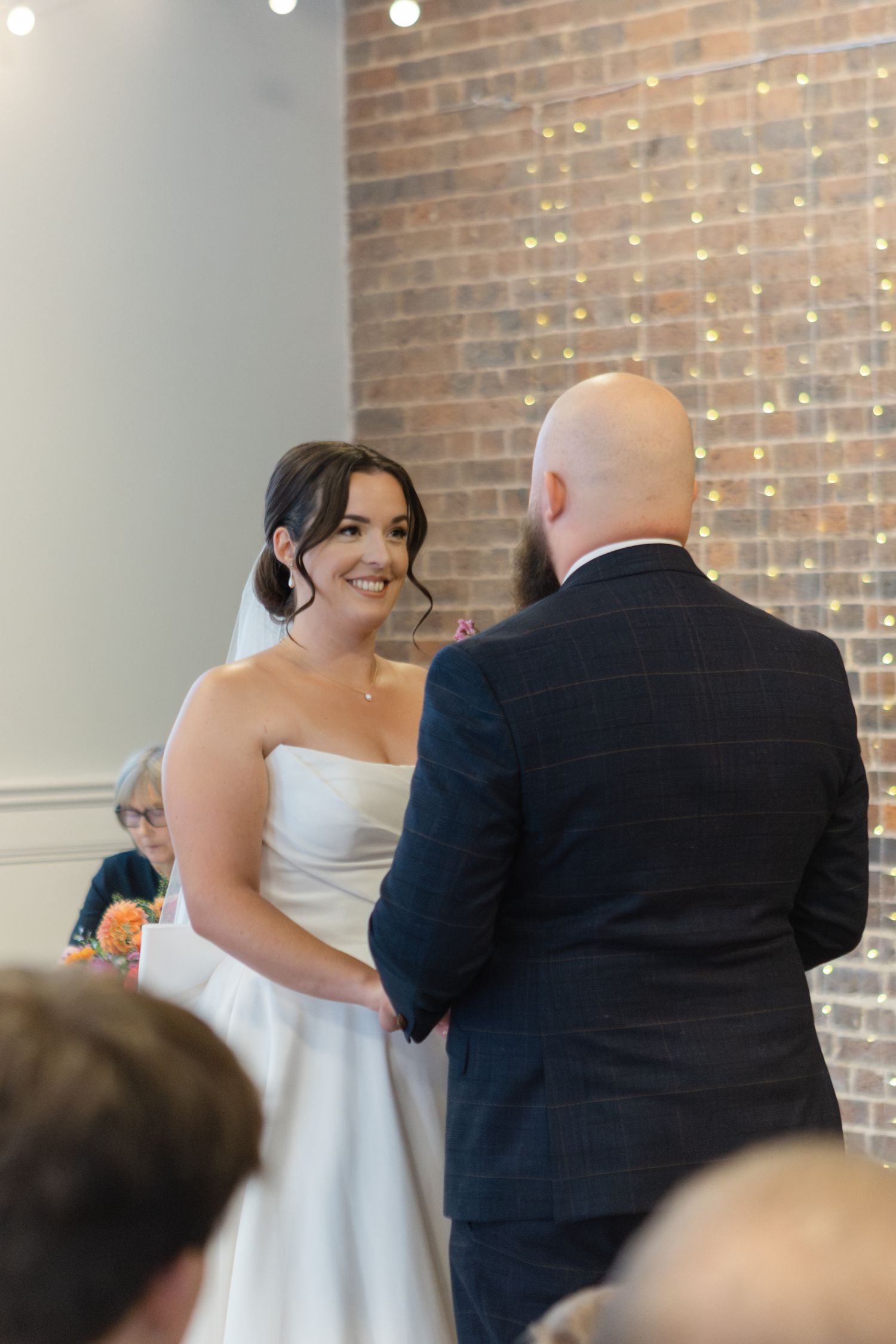 Wedding ceremony in a brick-walled venue with couple exchanging vows.