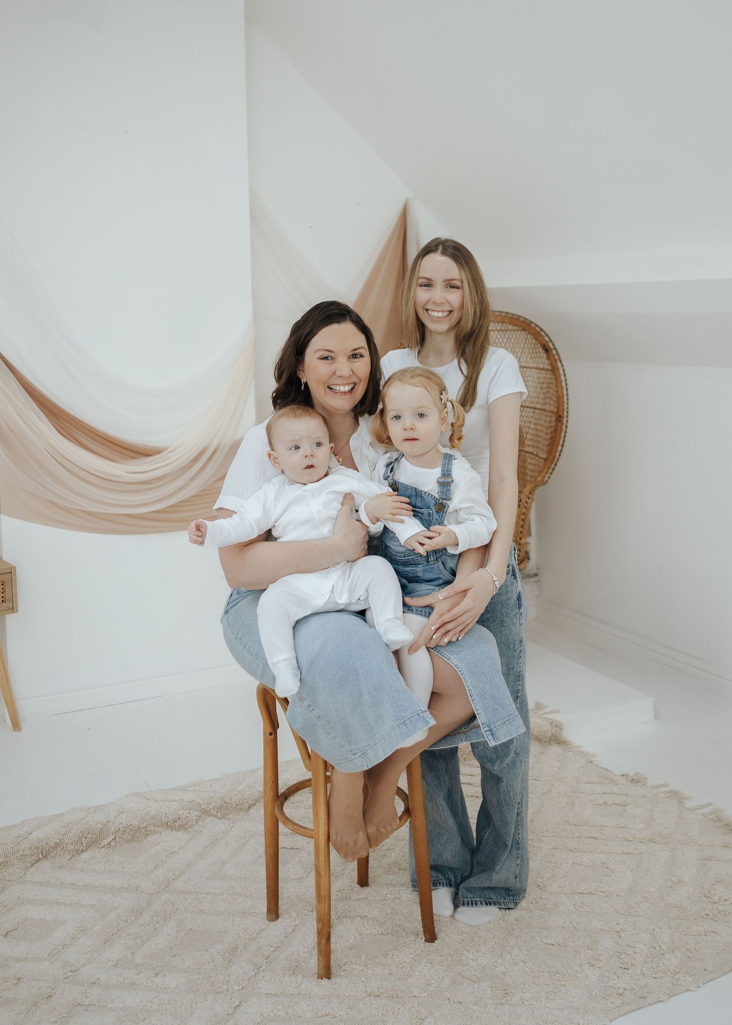 Family portrait with everyone wearing matching white tops and blue jeans in a bright studio setting.