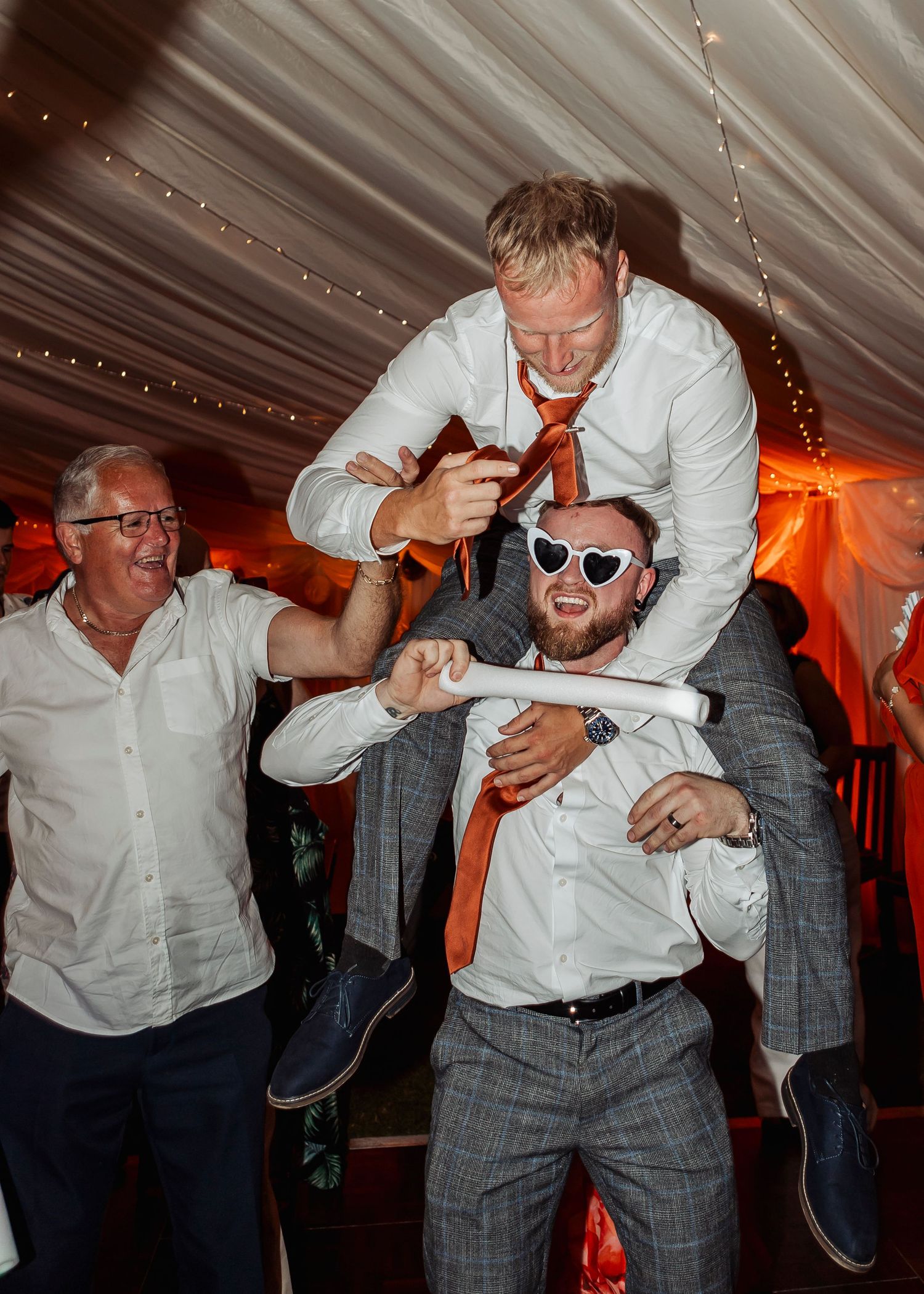 Fun reception moments showing guests dancing and celebrating under a white tent with string lights.