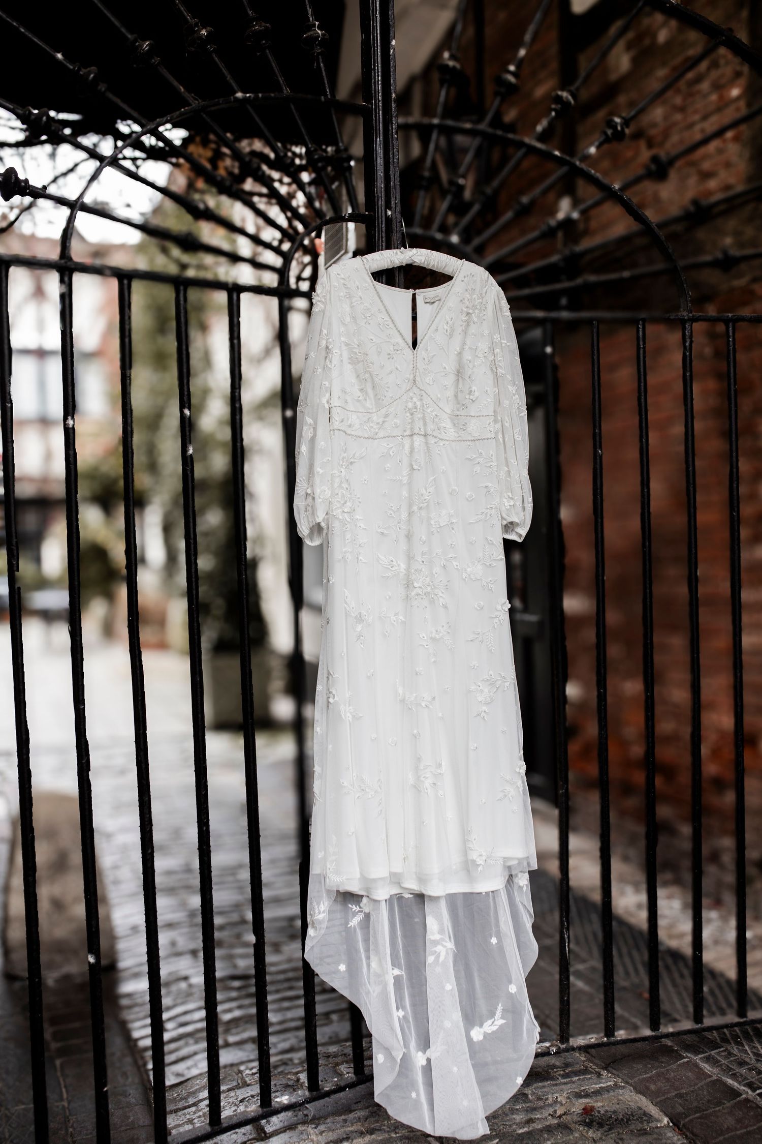A white lace wedding dress hangs dramatically against an ornate iron gate.