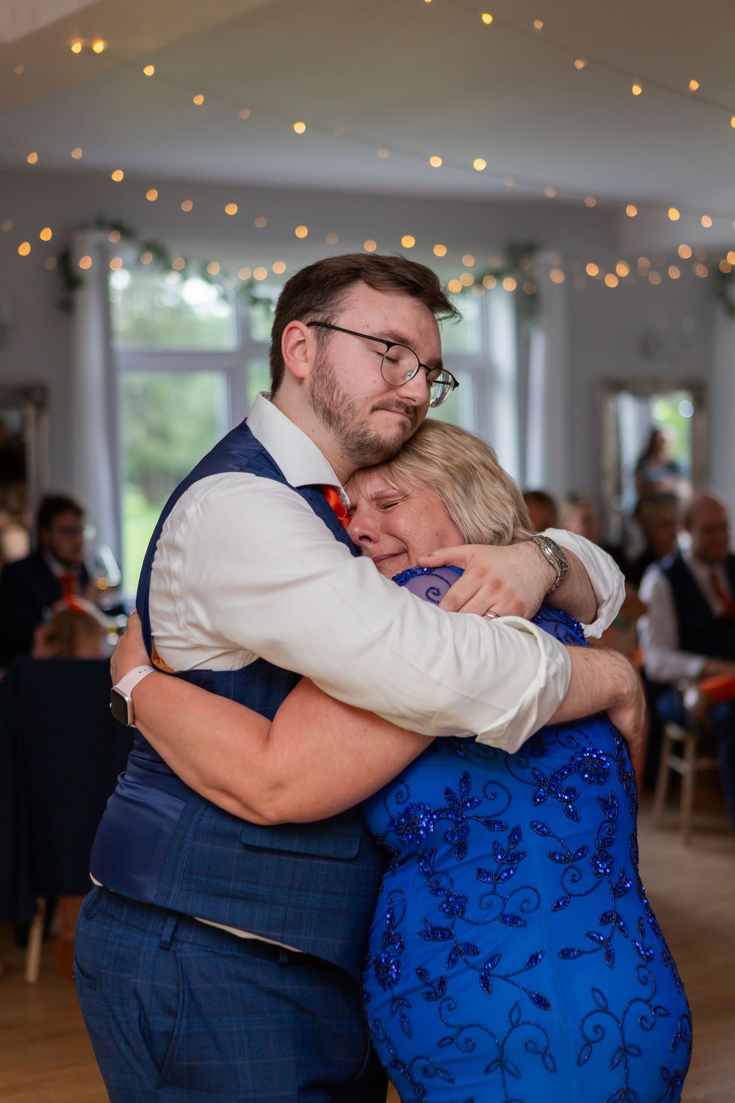 Tender dance moment captured between two people under string lights at a wedding celebration.