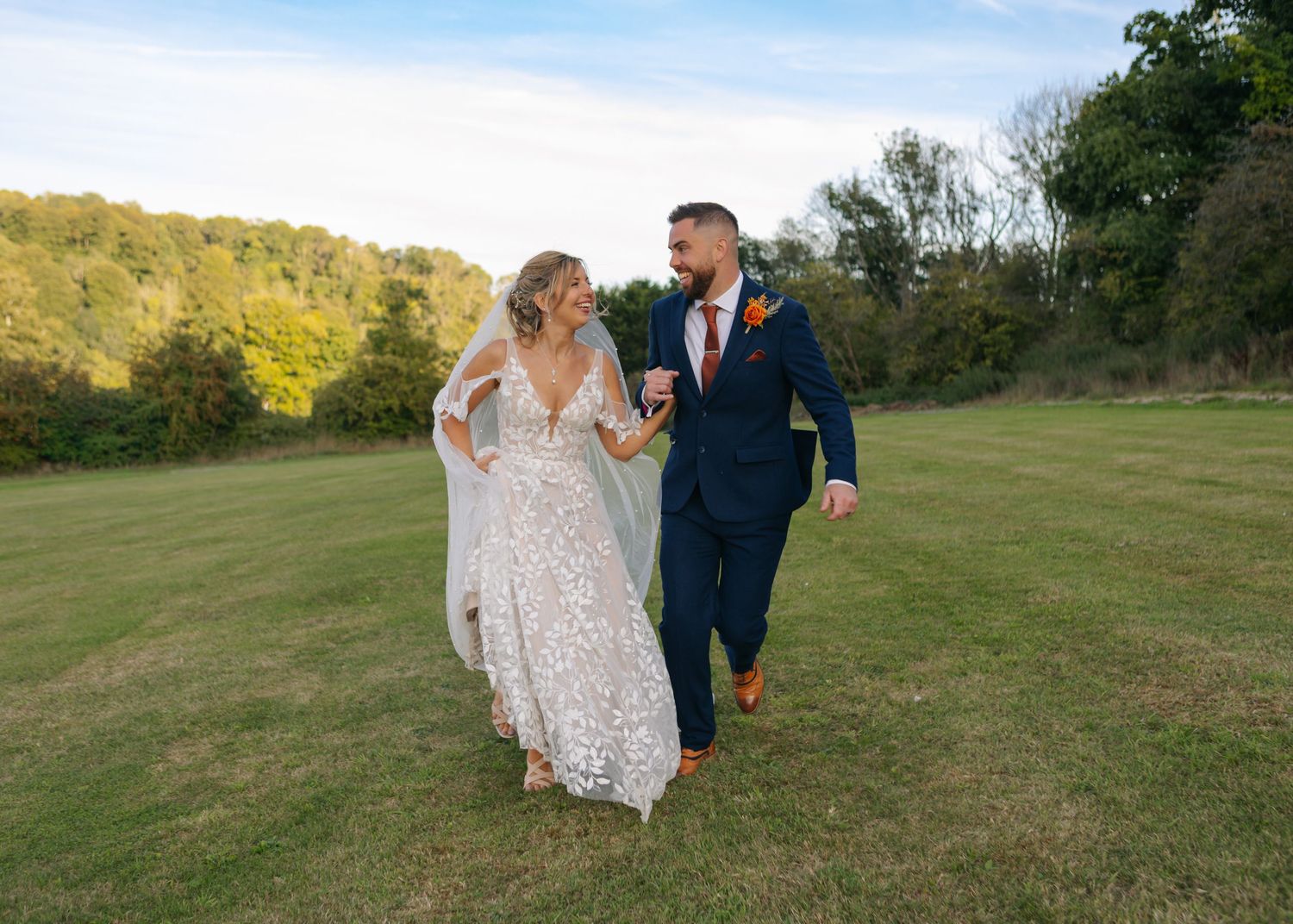 A joyful couple running through a sunlit field in wedding attire.