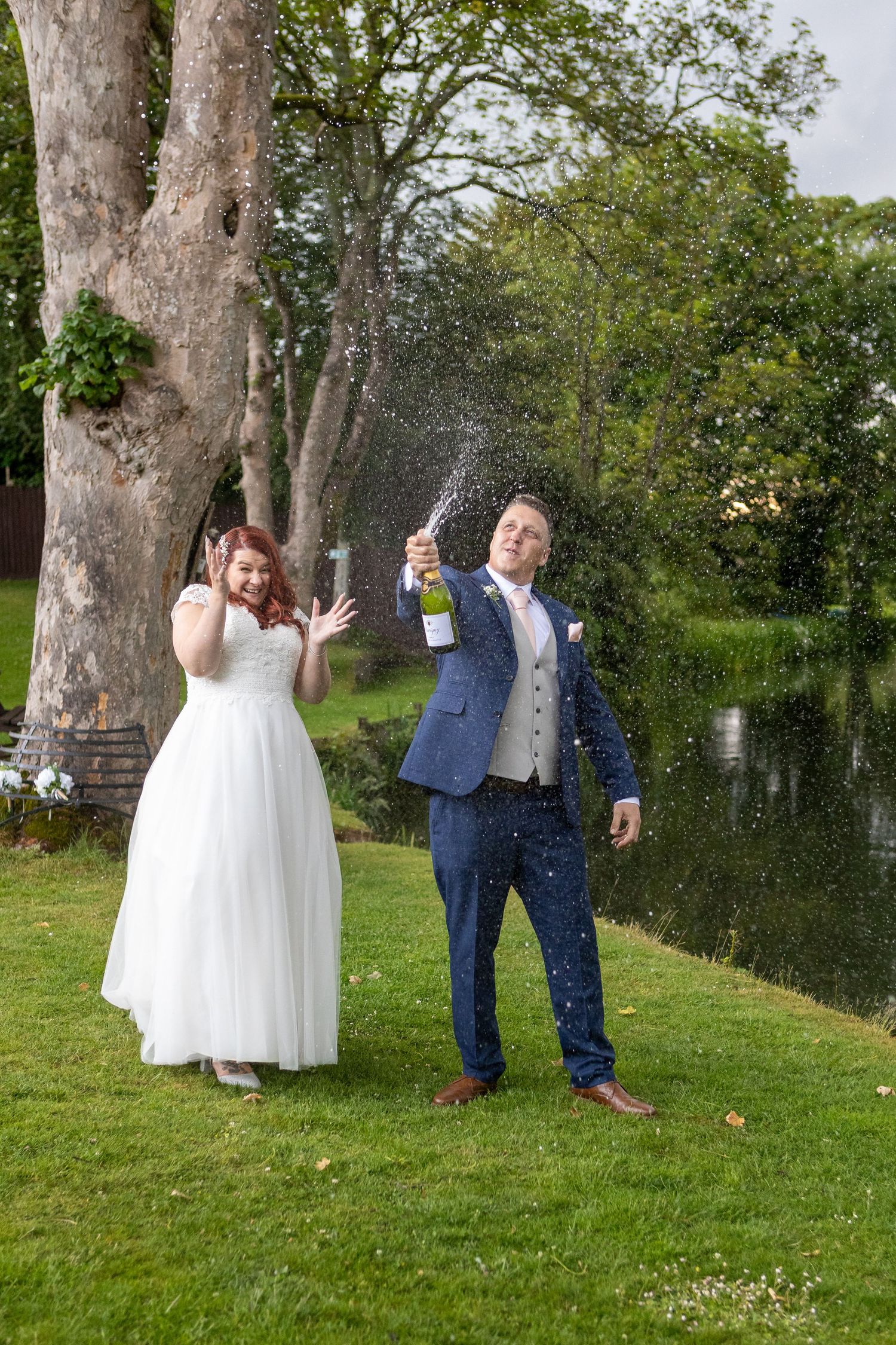 Newlyweds share a fun moment outdoors as confetti falls around them near a lake.