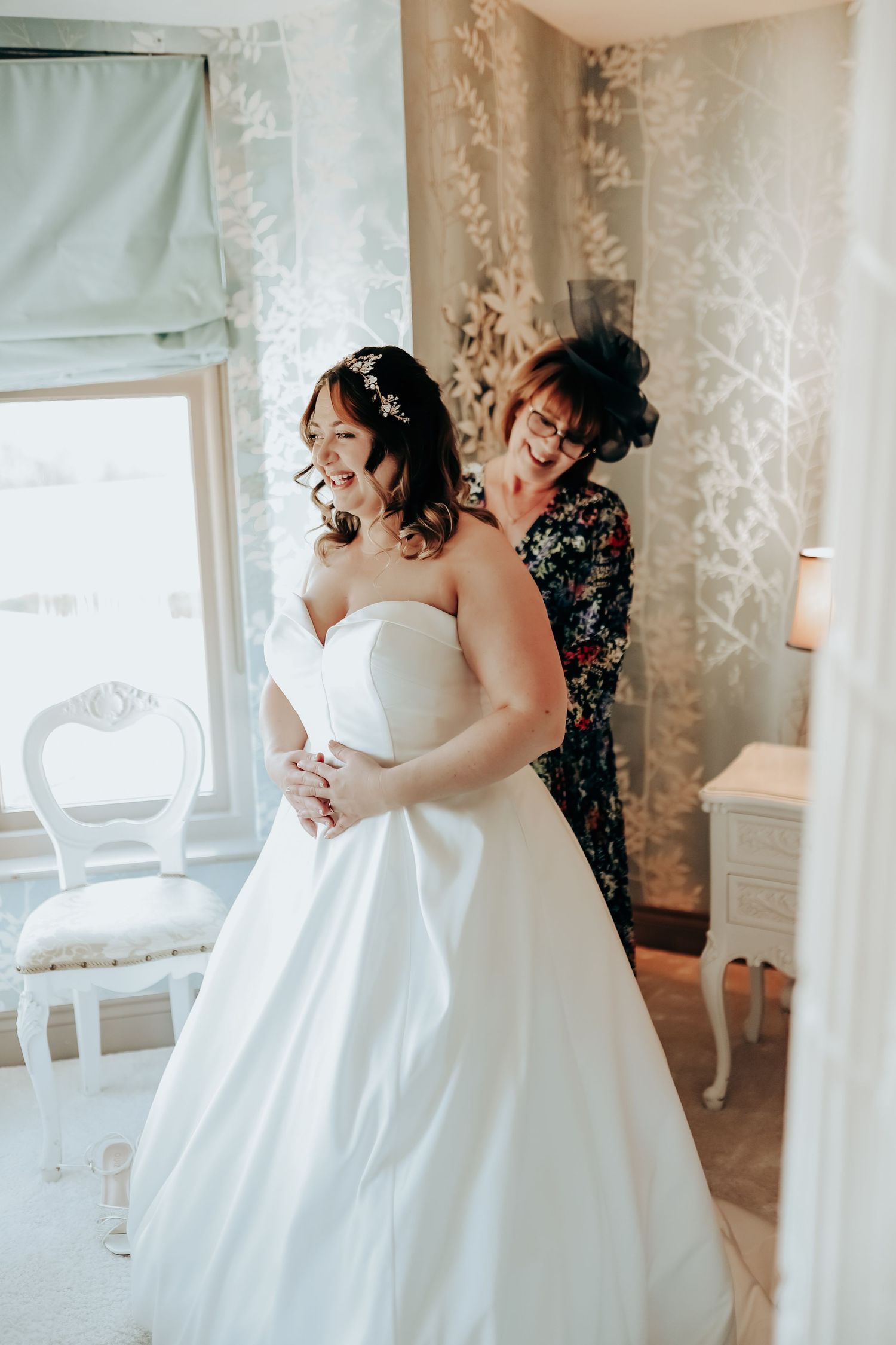 Elegant white wedding dresses displayed in a bridal boutique with silver wallpaper.
