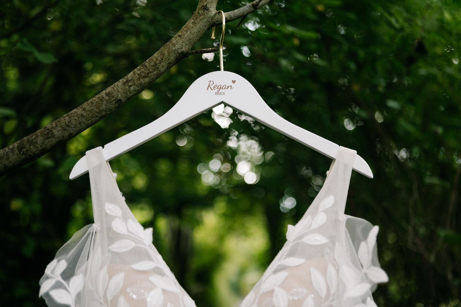 White wedding dress details hanging against natural greenery backdrop.