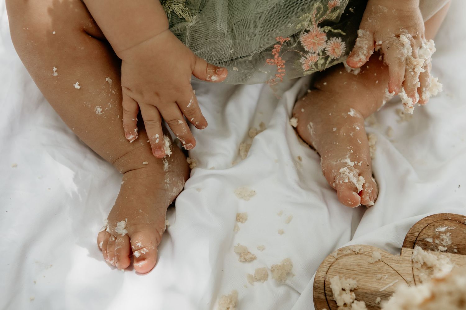 Close-up of tiny feet and hands playing with cake frosting on a white surface.