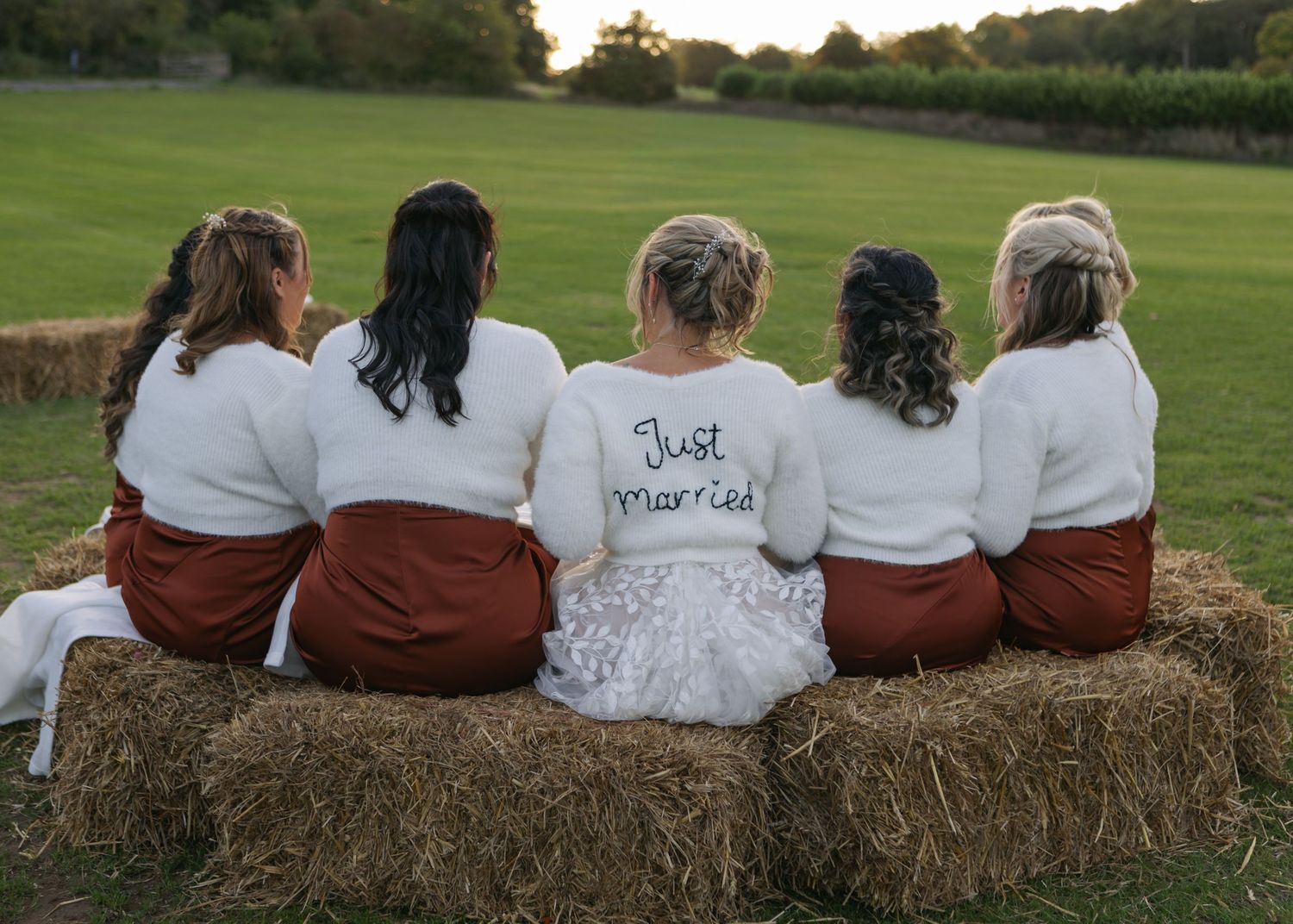 Bridesmaids in matching outfits sitting on hay bales with customized shirts.