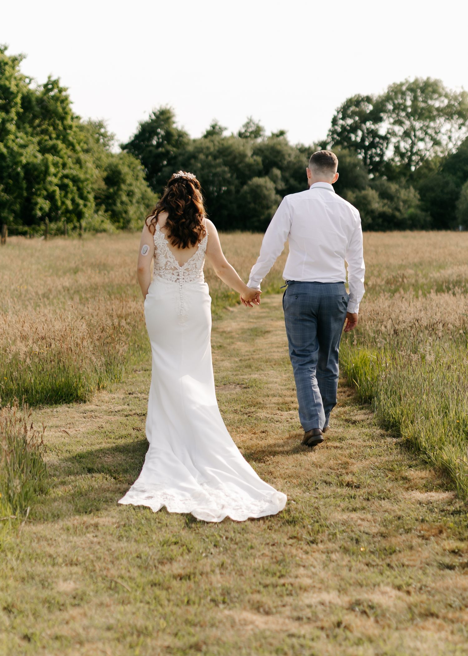 Newlyweds walking hand in hand through a rustic meadow with flowing wedding dress.