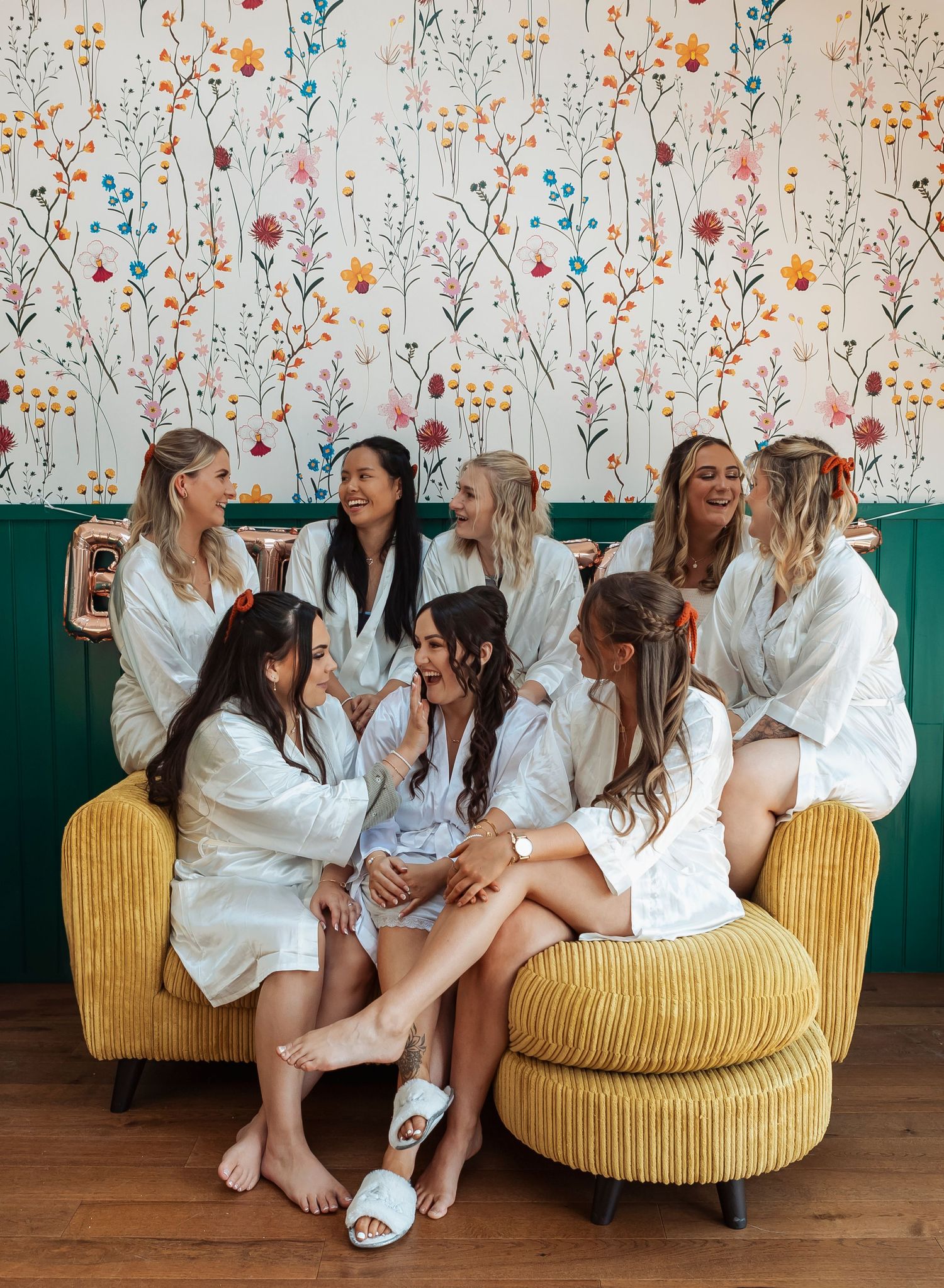 A group in white robes sitting on a yellow couch against a floral wallpaper background.