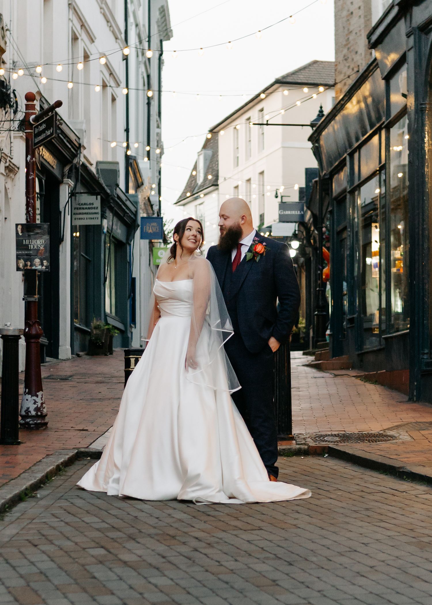 Romantic wedding photos taken in a charming cobblestone alley with string lights overhead.