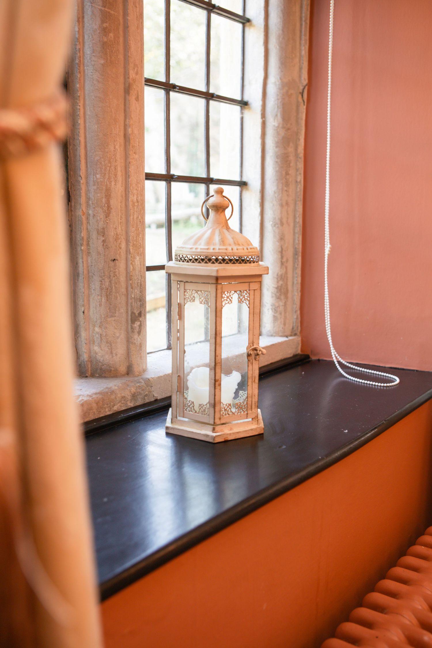 Decorative white lantern sits on a rustic windowsill with coral-colored walls.