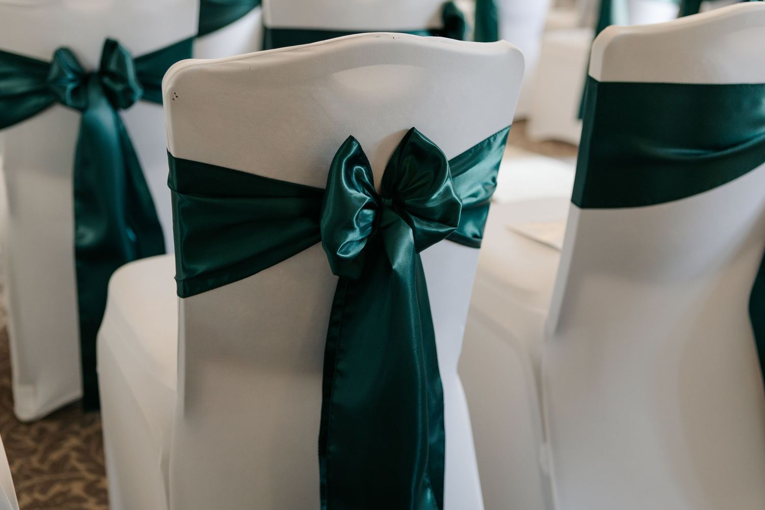 Chair covers with dark green satin bows lined up for a wedding ceremony.