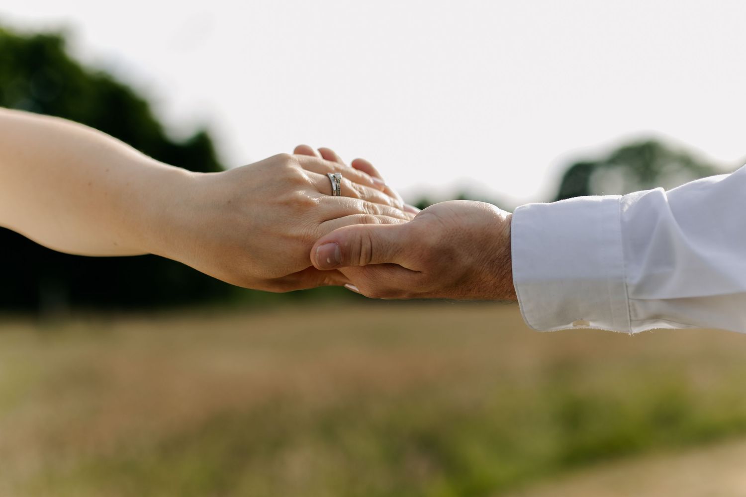Close-up shot of hands with wedding rings in natural outdoor lighting.