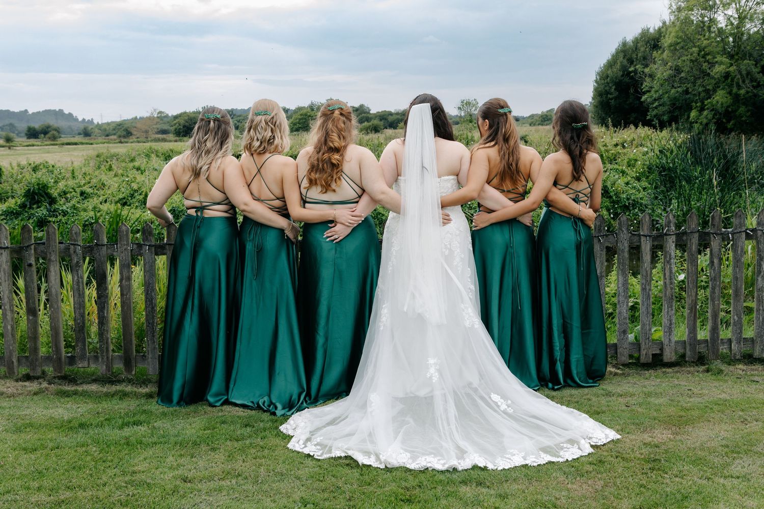 Wedding party in emerald green dresses and white gown posing in garden setting.