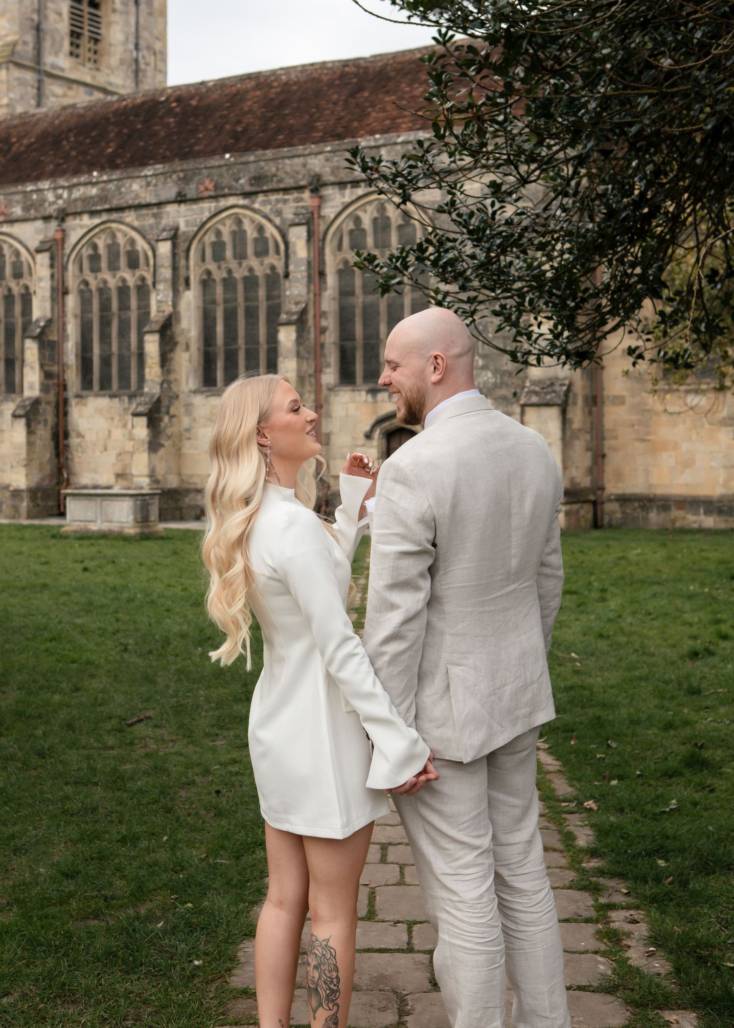 Couple in matching light colored outfits share romantic moment outside stone church.