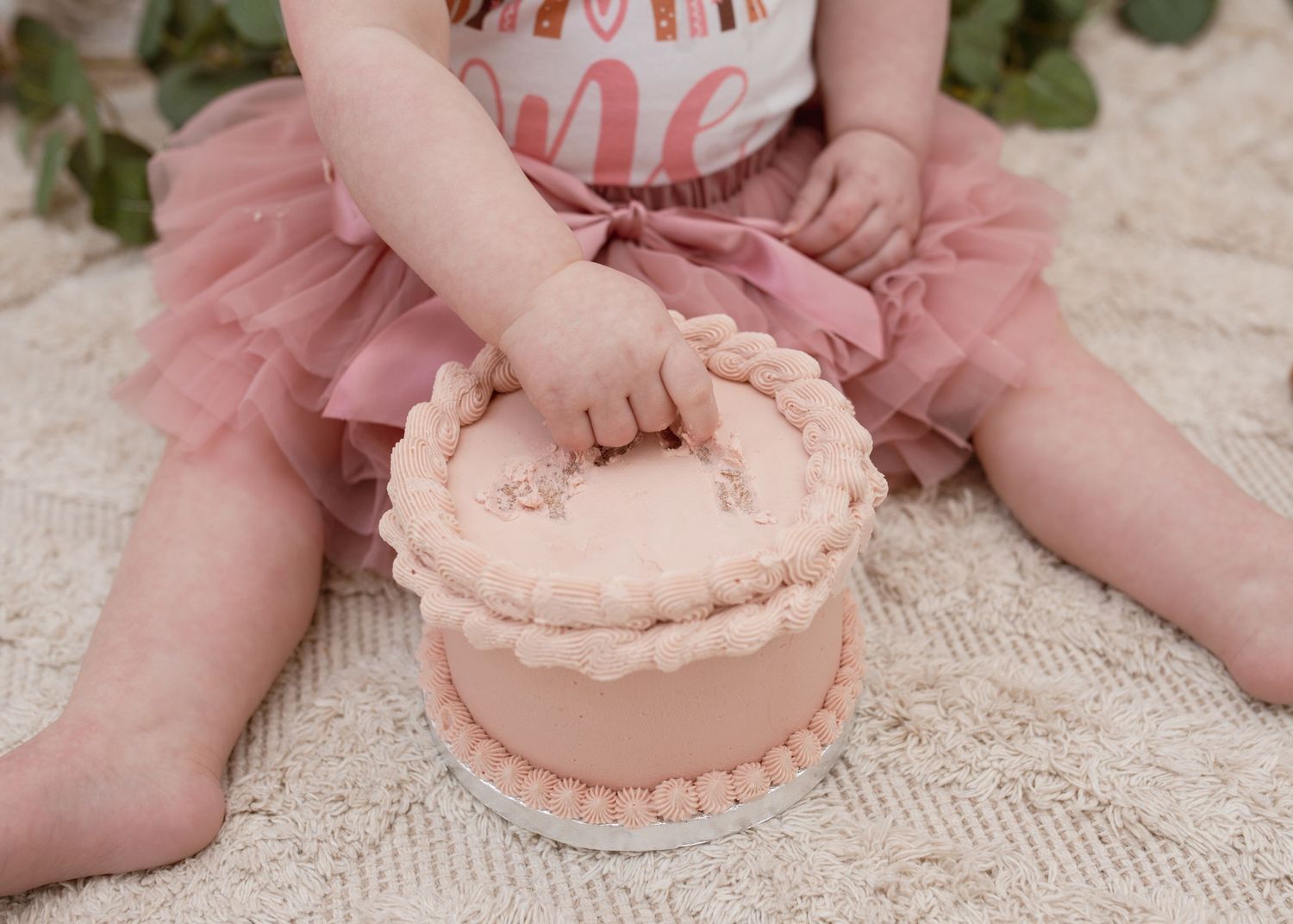 Pink frosted cake being explored during first birthday cake smash photoshoot.