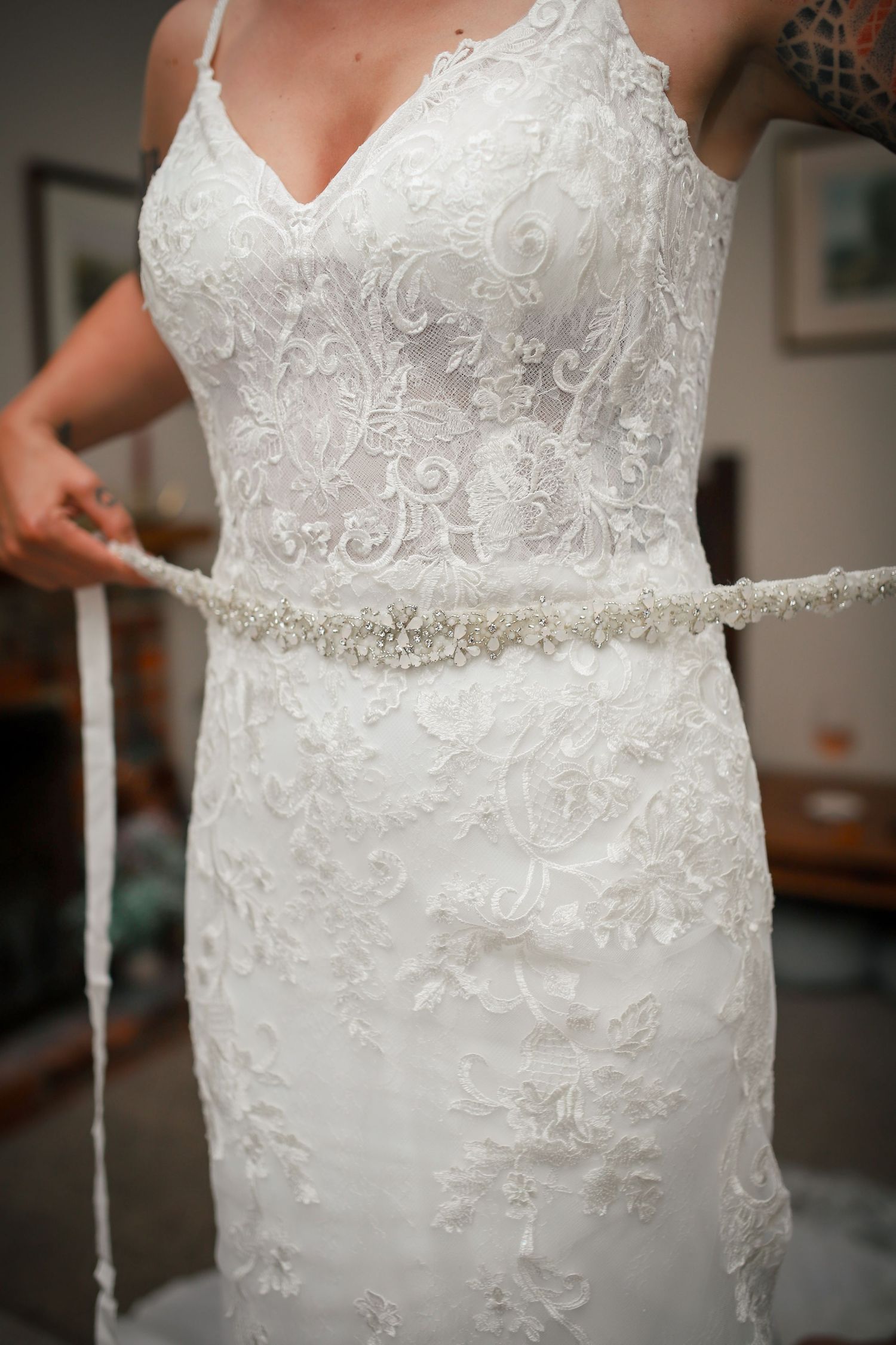 Elegant white lace wedding dress with beaded belt detail shown in close-up.