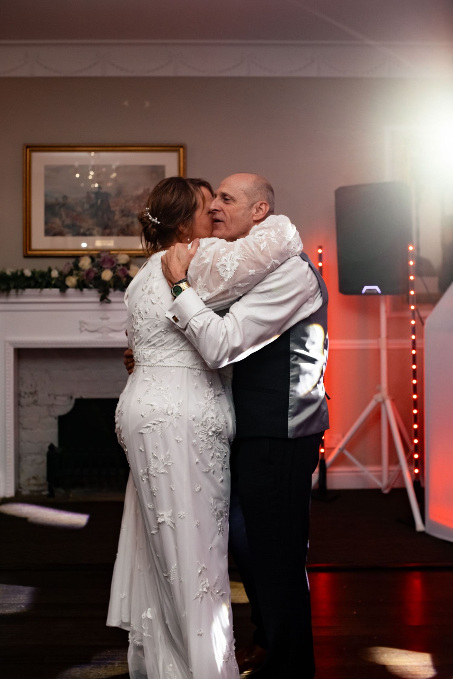 Newlyweds share an intimate slow dance at their wedding reception with red accent lighting.