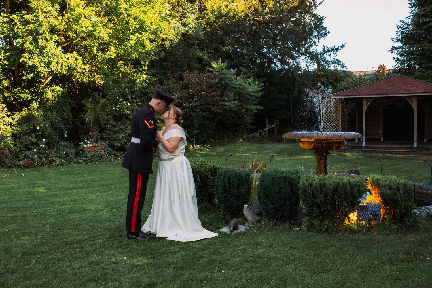 Outdoor wedding ceremony setup in a lush garden with golden sunlight filtering through trees.