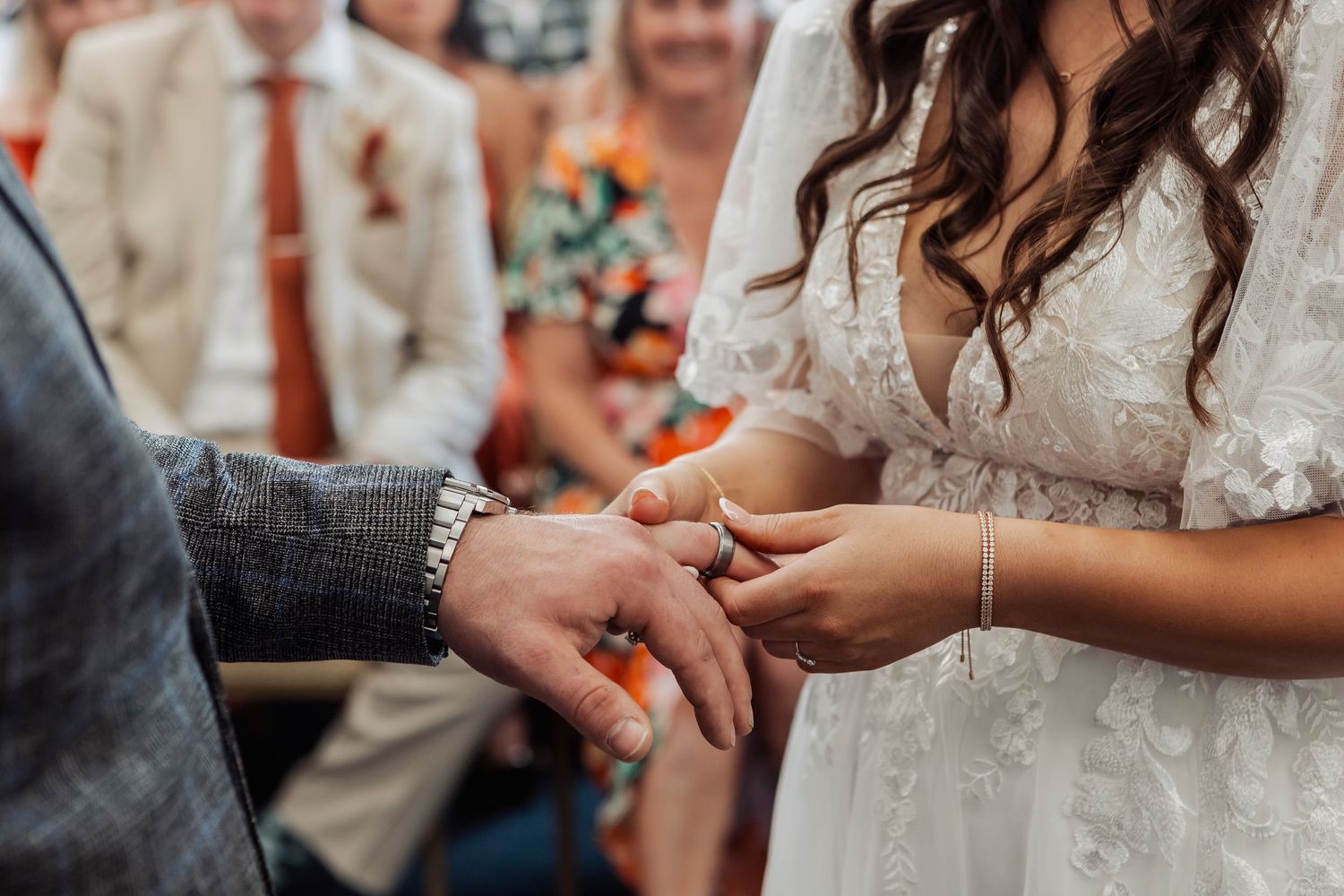 Close-up of wedding ring exchange between couple wearing traditional wedding attire.