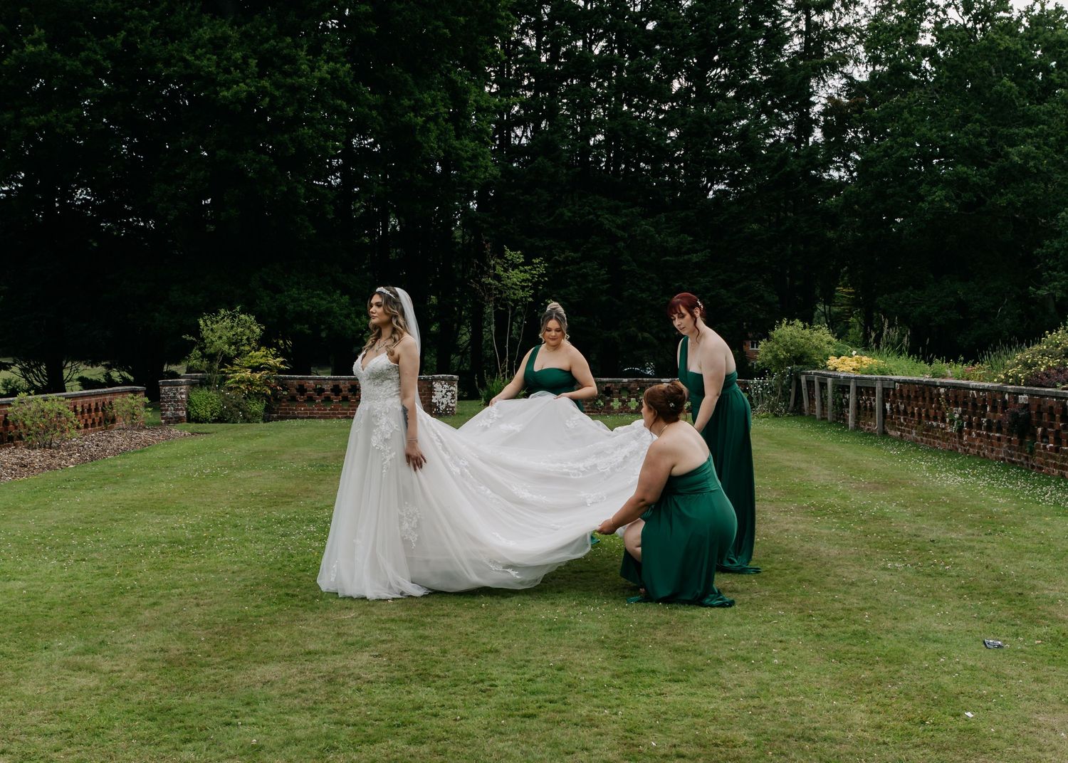 Wedding party in emerald green and white dresses posing on a lush green lawn.