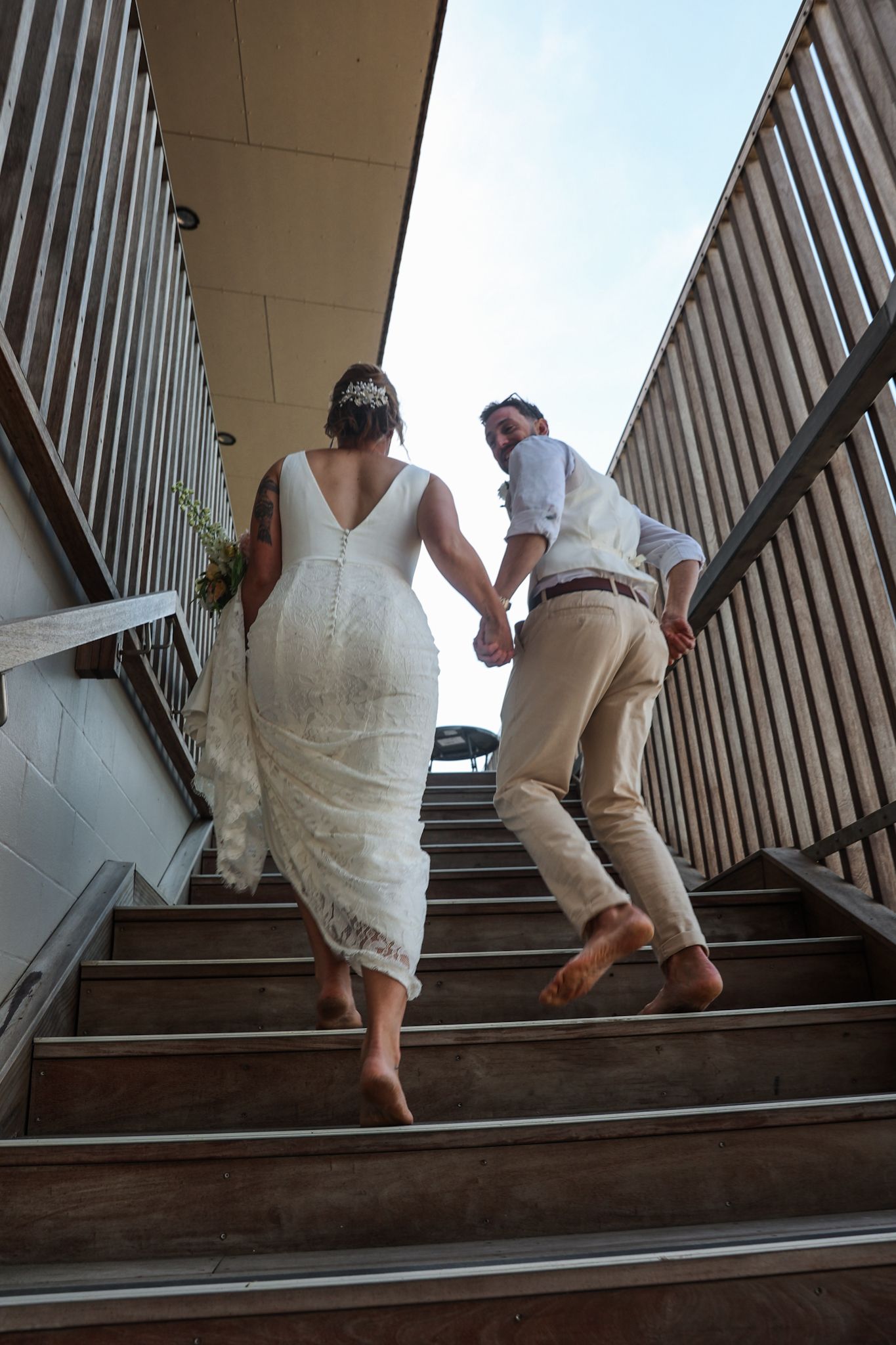 Bride and groom running up the stairs to arrive at their reception party.