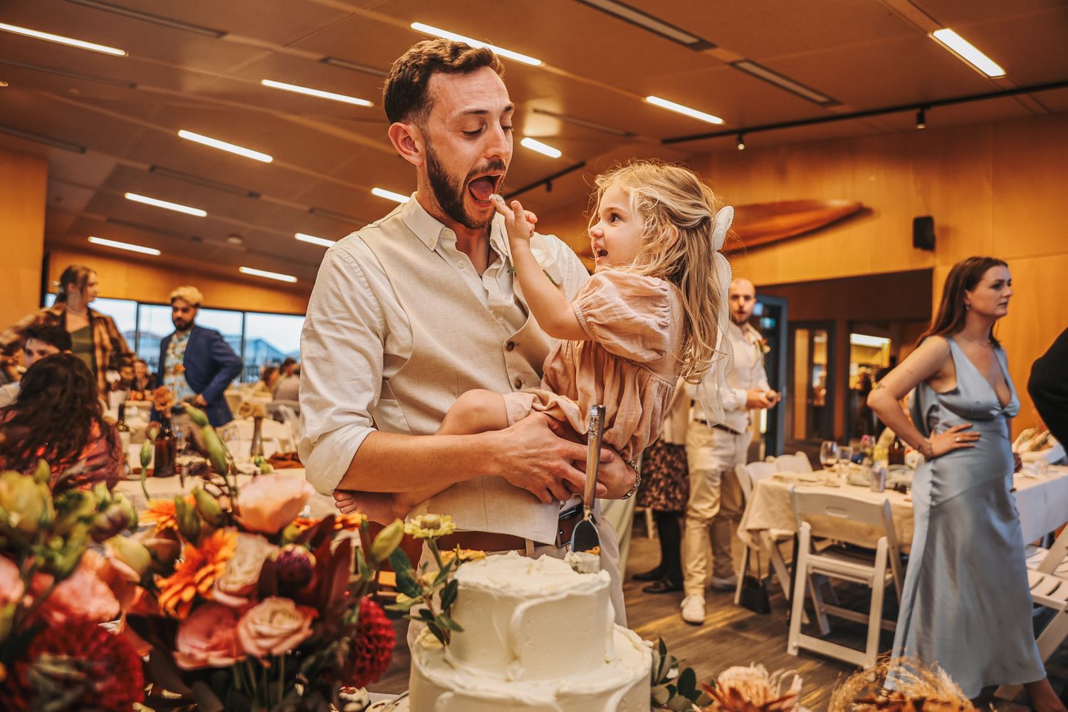 Groom and young daughter enjoying frosting from wedding cake