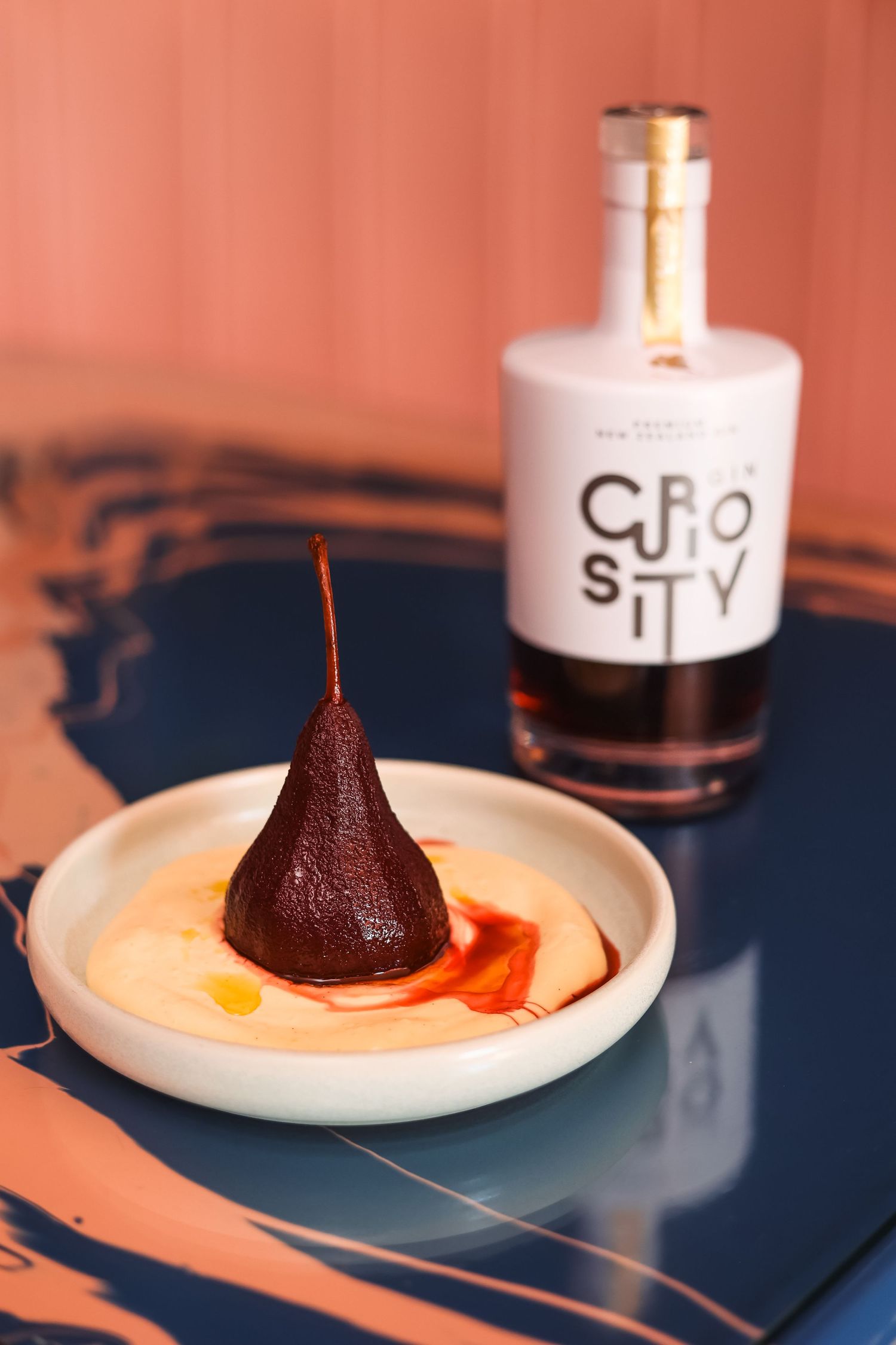 Poached sloe-gin pear dessert dish with a bottle of Curiosity sloe-gin