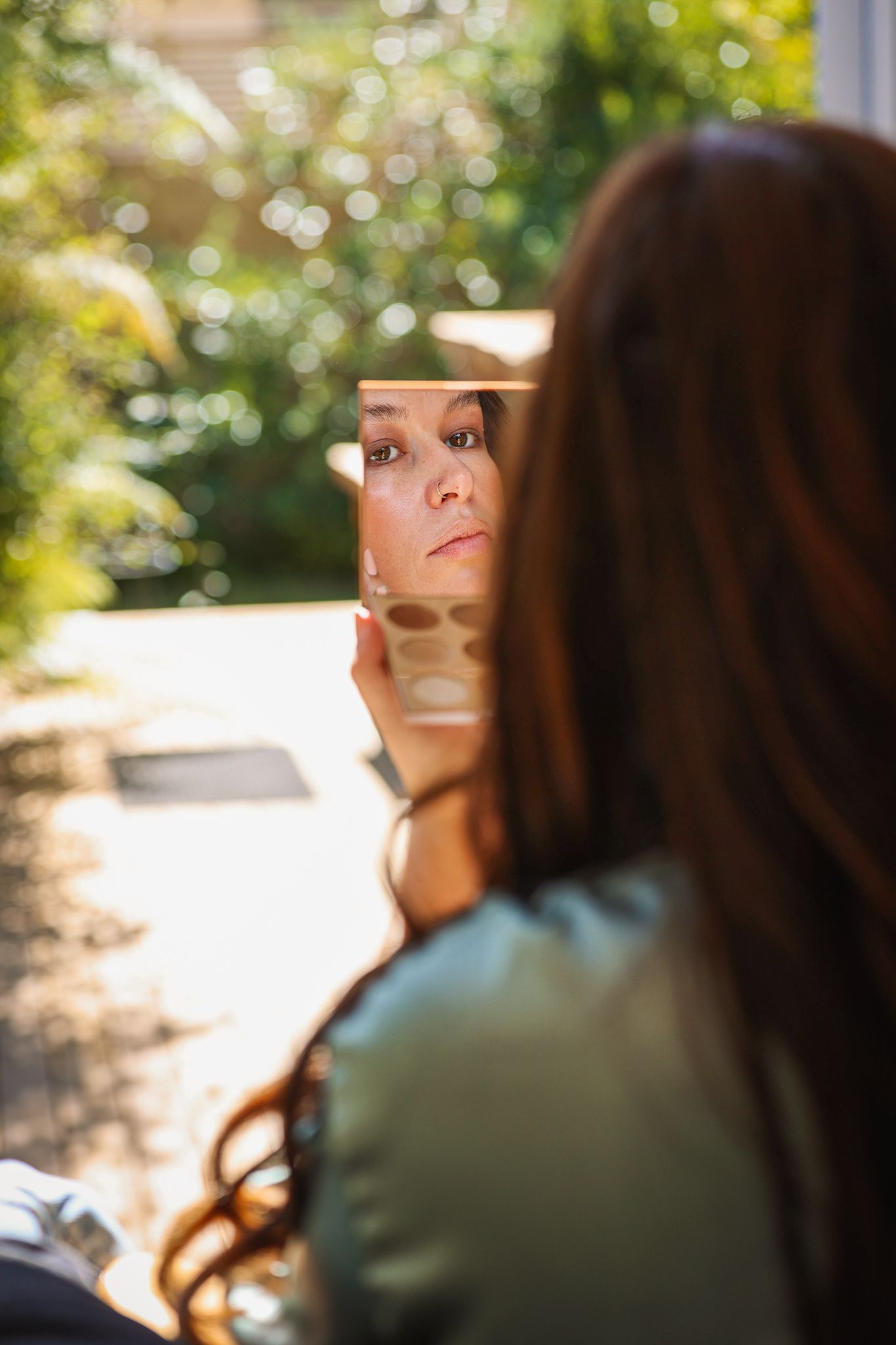 A bridesmaid captured through her eyeshadow palate mirror as she applies her makeup.
