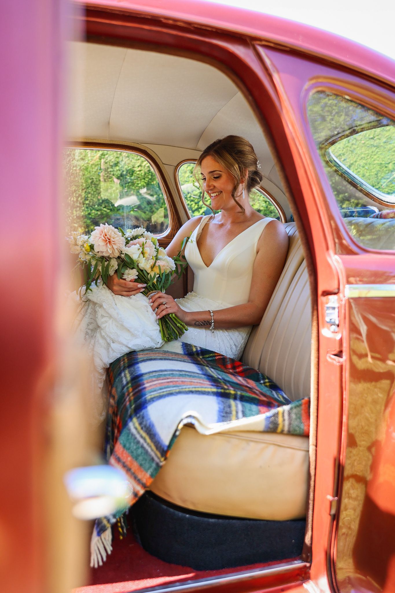 Bride staring down at her bouquet of flowers from inside the classic car on the way to the wedding
